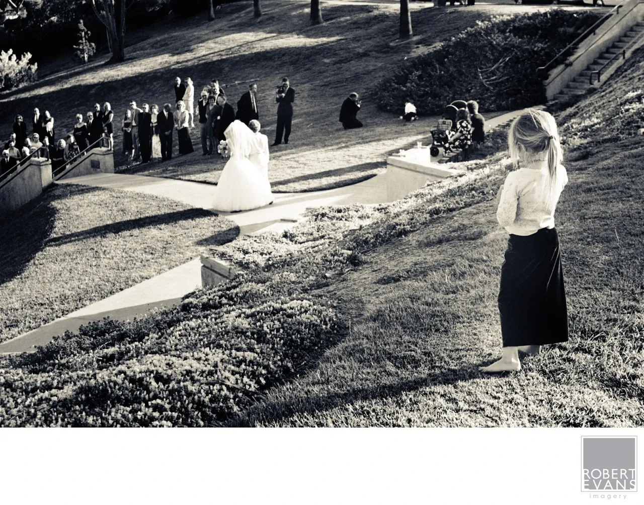 A wedding ceremony unfolds on a landscaped slope, photographed from above in black and white.