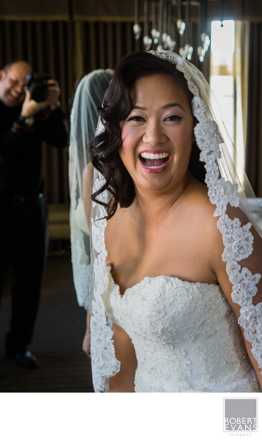A bride laughs openly beneath her veil while standing in a doorway.