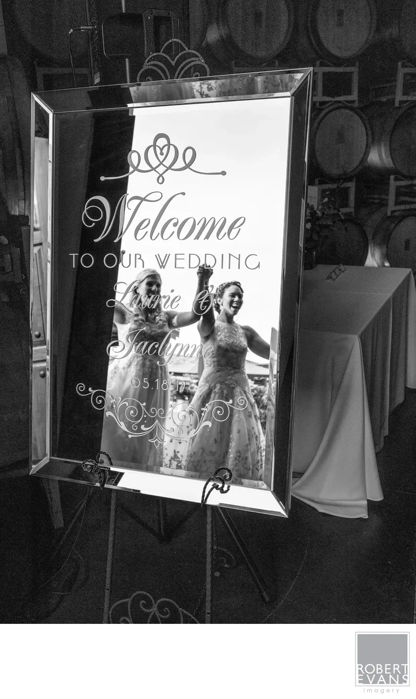 Women in wedding attire are reflected in a decorative welcome mirror in black and white.
