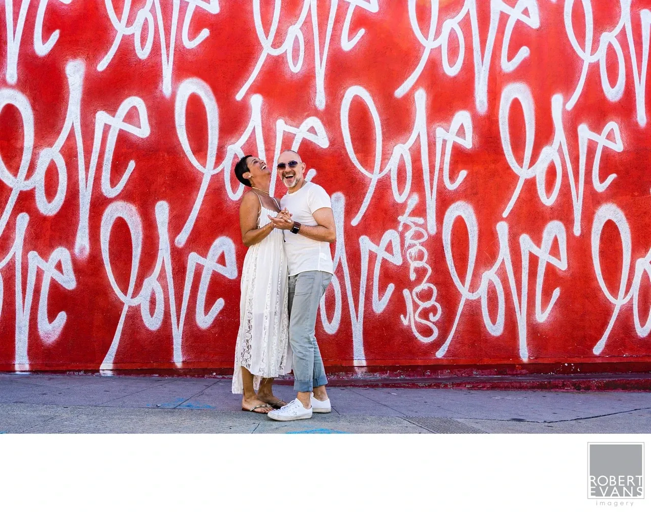 A couple embraces against a vivid red wall covered with the word love.