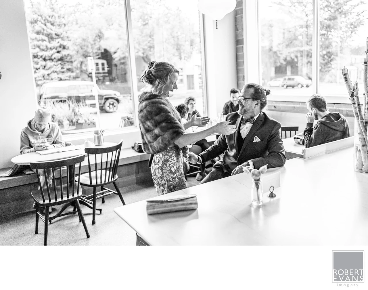 People talk together in a bright café interior in a documentary black-and-white photograph.