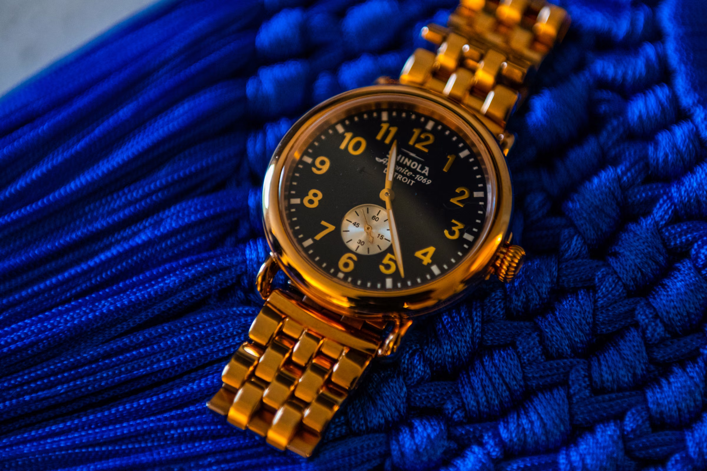 Gold Shinola watch with a black face photographed against blue fabric