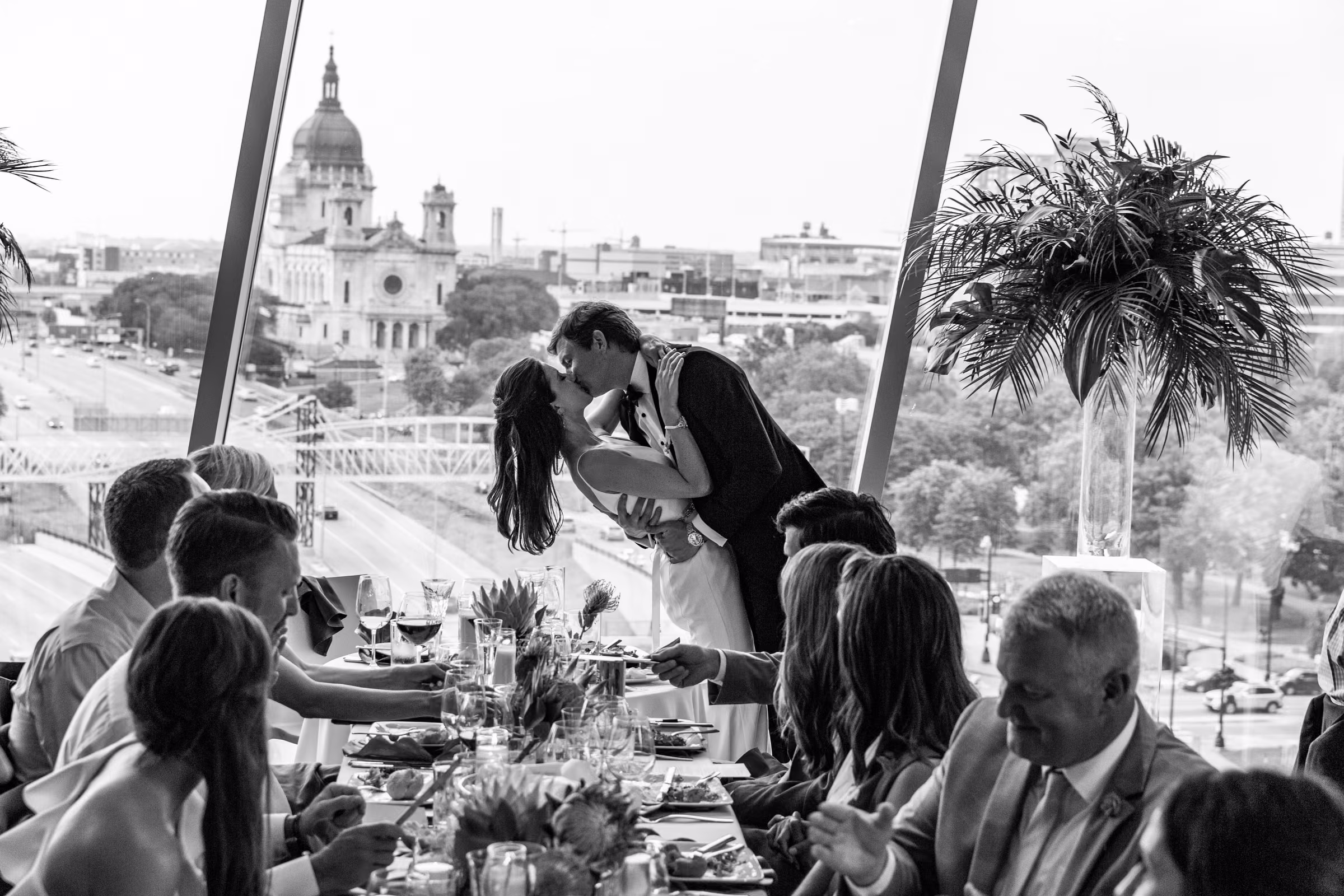Ali and Drew rise to kiss at their reception table with the Basilica of Saint Mary visible through the windows