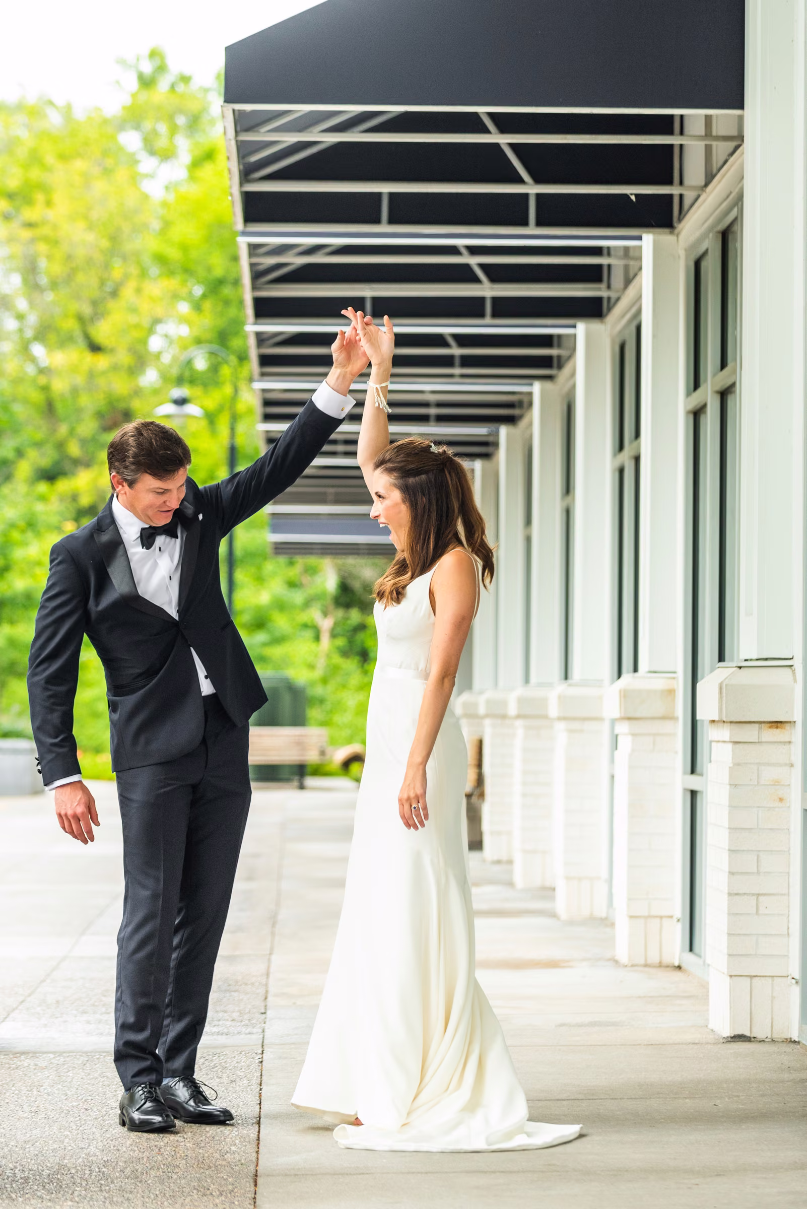 Drew raises Ali’s hand as she turns beneath the awning outside The Hotel Landing