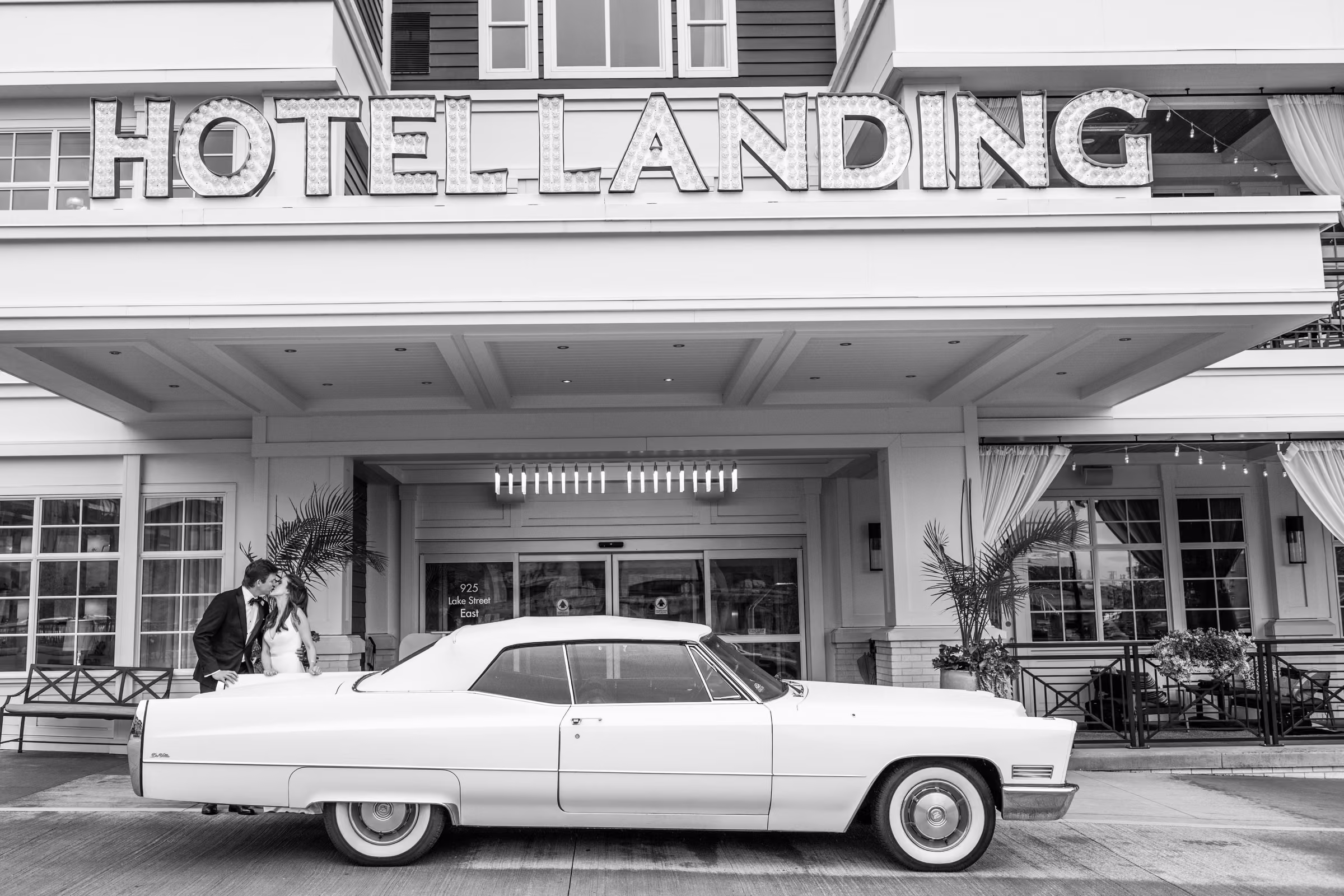 A white vintage Cadillac sits outside The Hotel Landing with Ali and Drew beside the hotel entrance