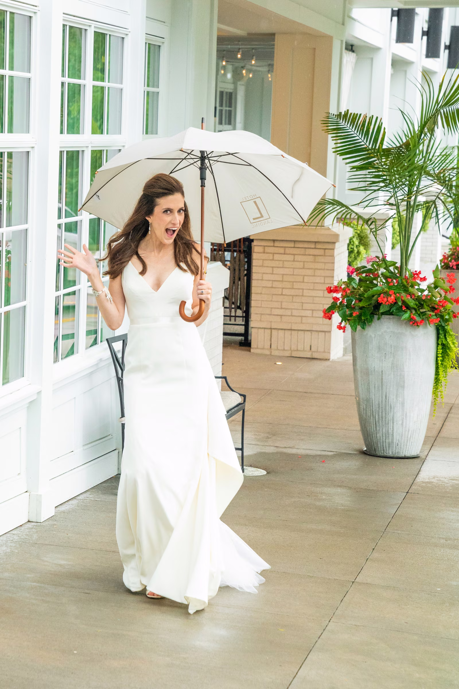 Ali steps out of The Hotel Landing in her wedding dress beneath a clear umbrella