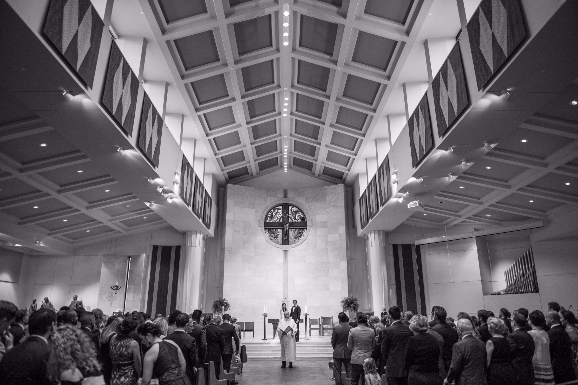 Wide black-and-white view of Ali and Drew’s ceremony beneath the skylights at St. Bartholomew Catholic Church