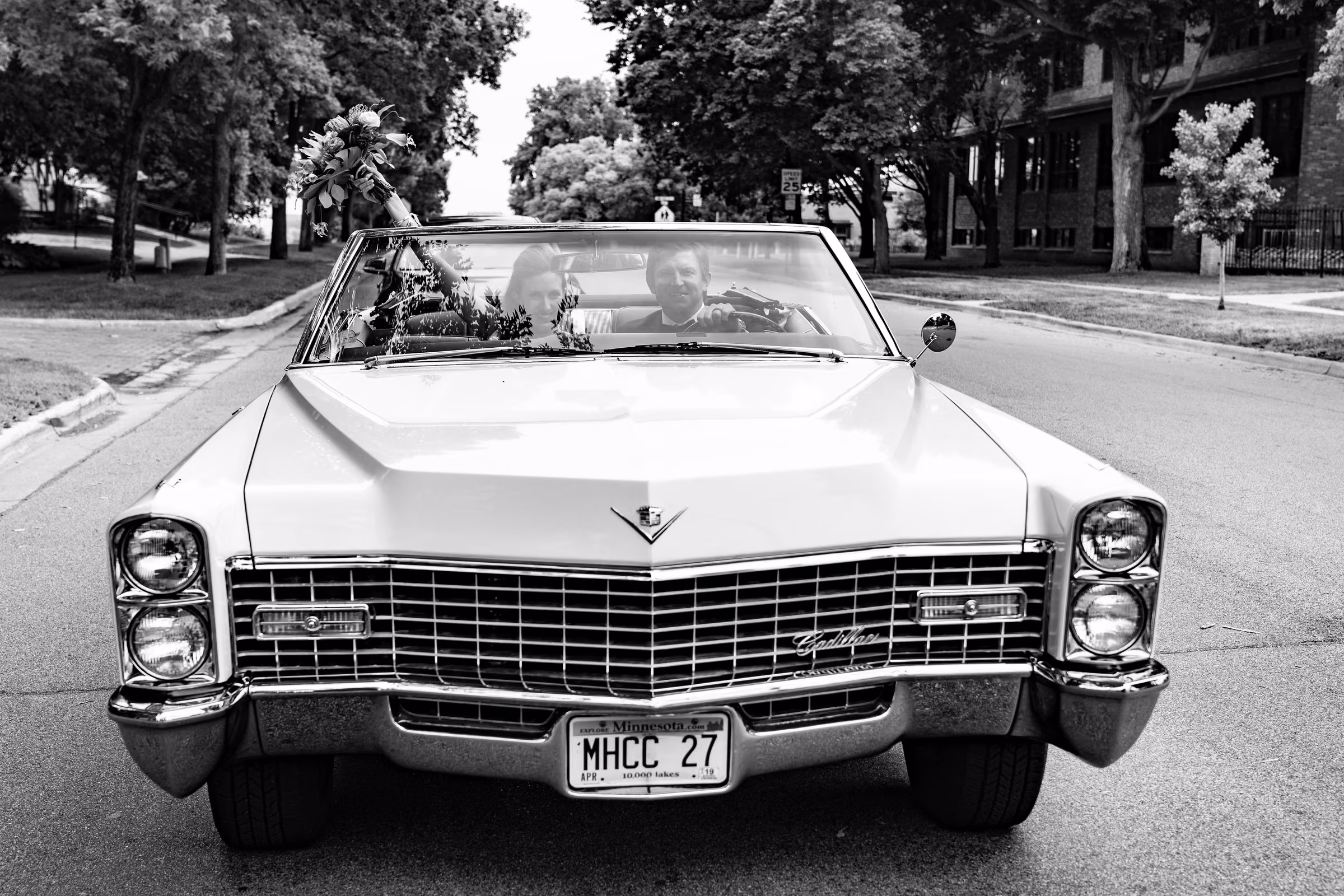 Ali and Drew ride through a tree-lined street in their white Cadillac convertible