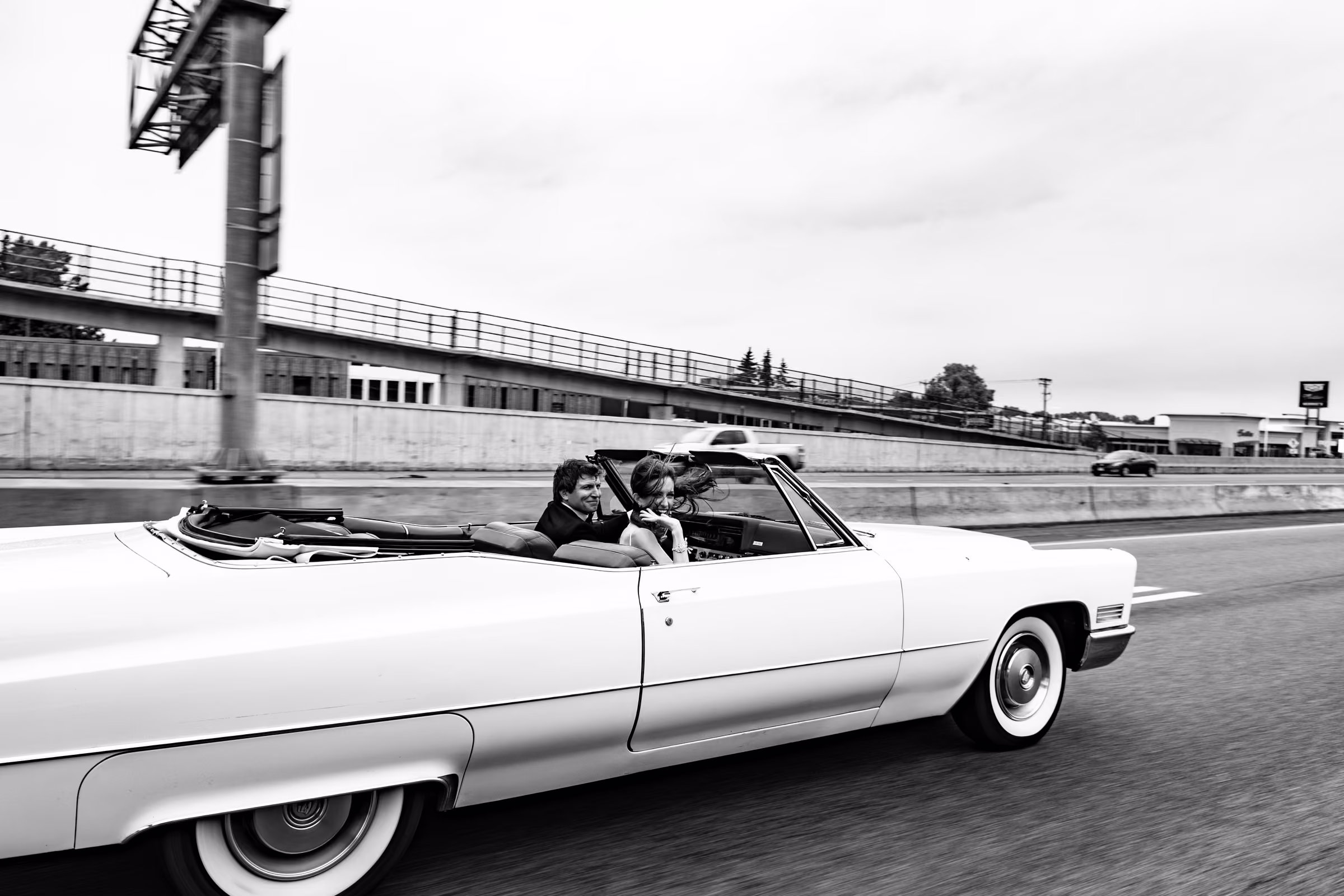 Side view of Ali and Drew riding in the white Cadillac convertible on the freeway