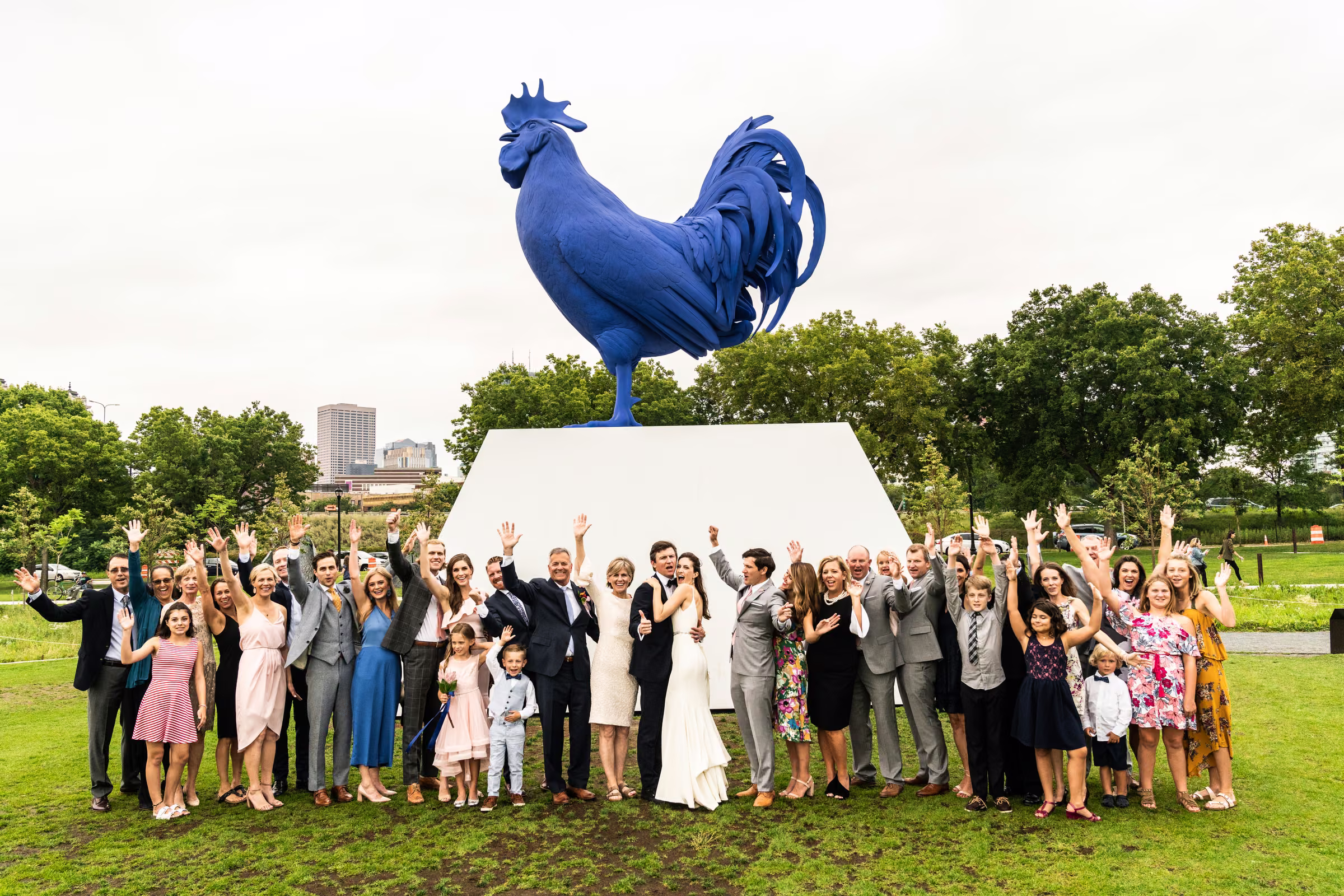 Ali, Drew, and family raise their arms beneath the giant blue rooster in the Minneapolis Sculpture Garden