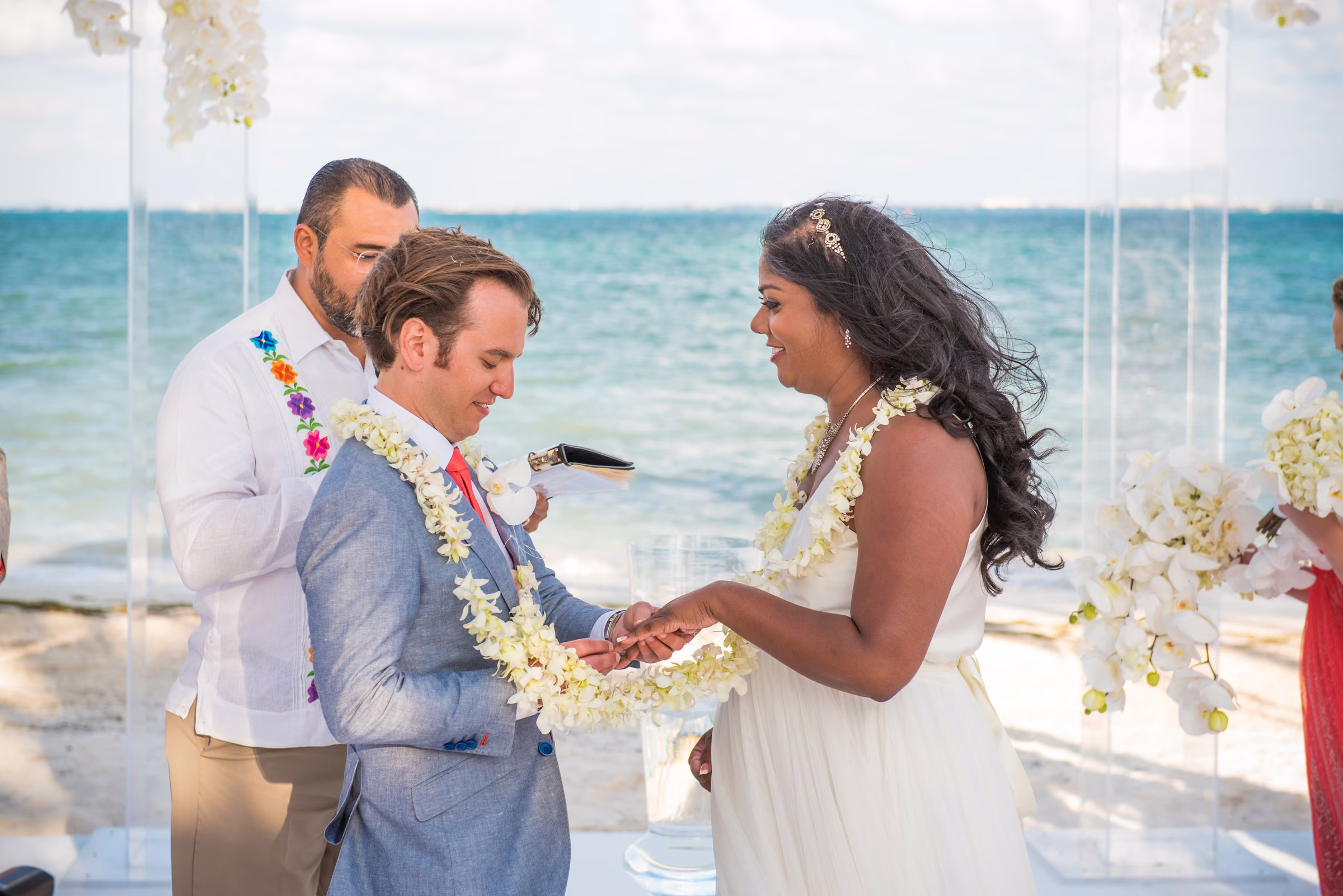 Avanti and Tony exchange rings beneath the ceremony canopy with the sea behind them