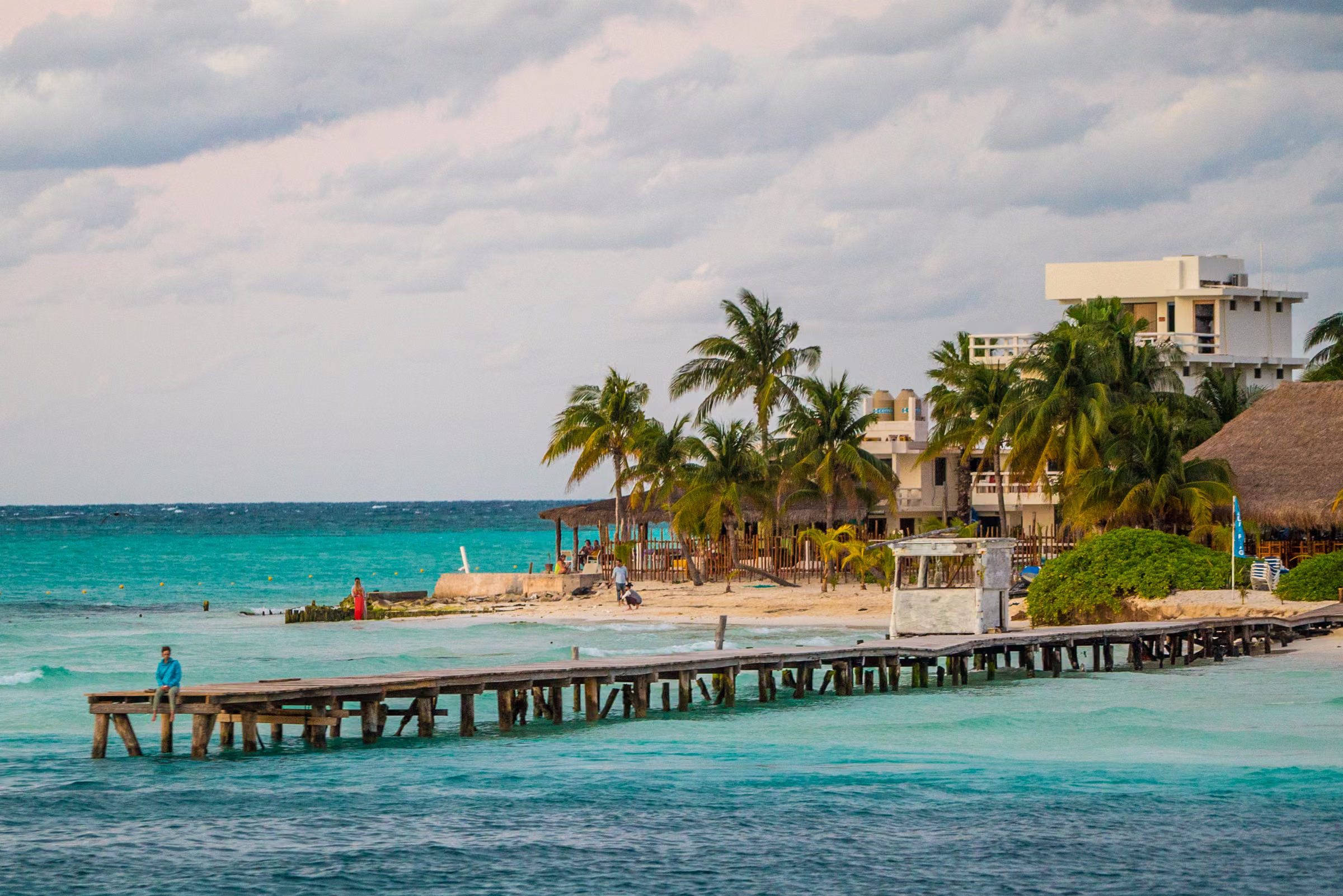 Turquoise water, a wooden pier, and palms along the tropical shoreline near Cancún