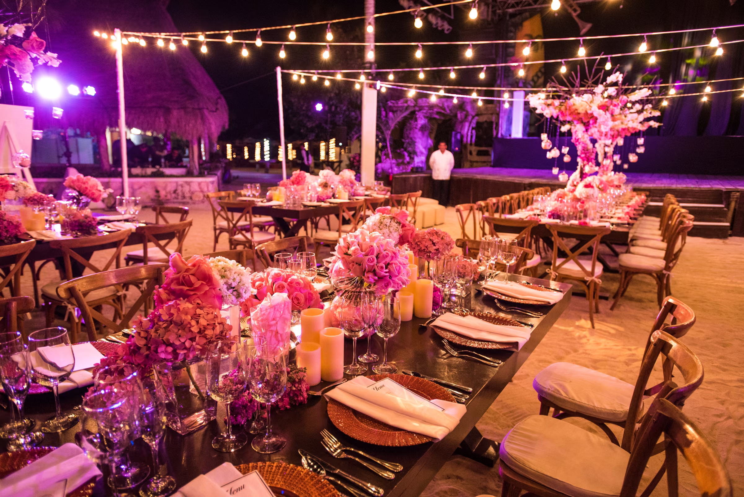 Pink flowers and candlelit place settings line the outdoor welcome dinner tables
