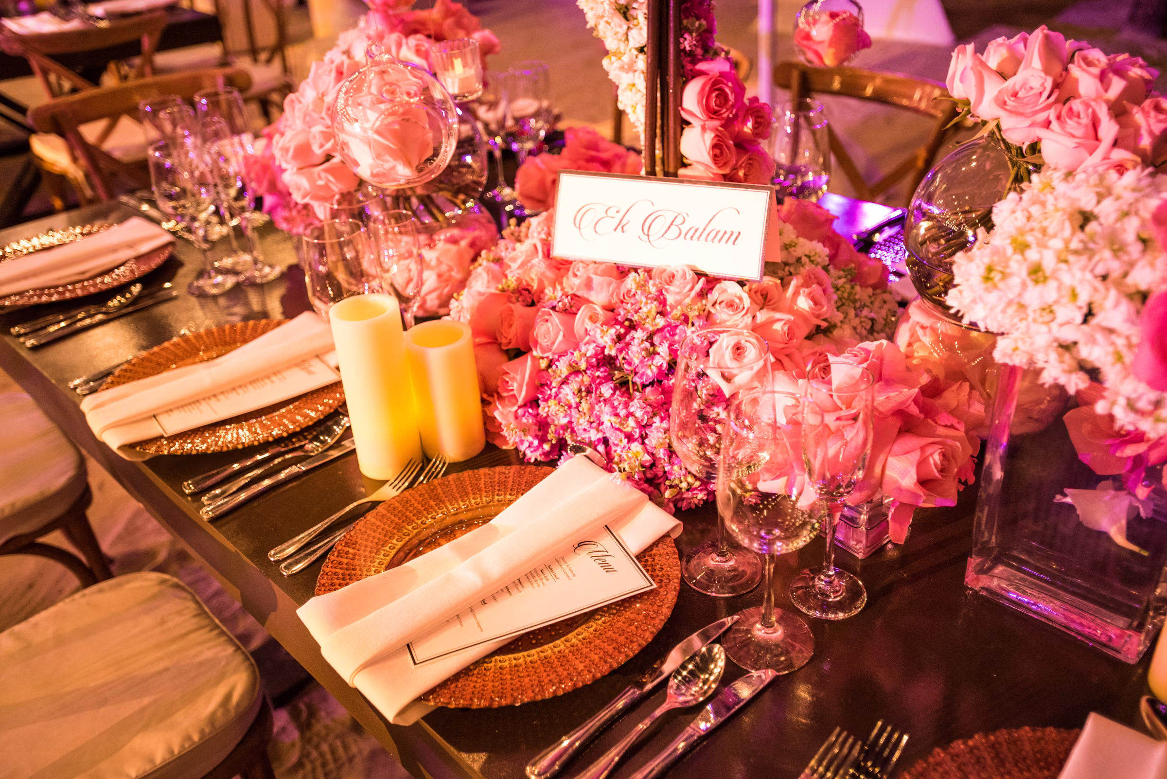 Pink floral arrangements, glassware, and folded napkins fill a welcome dinner table