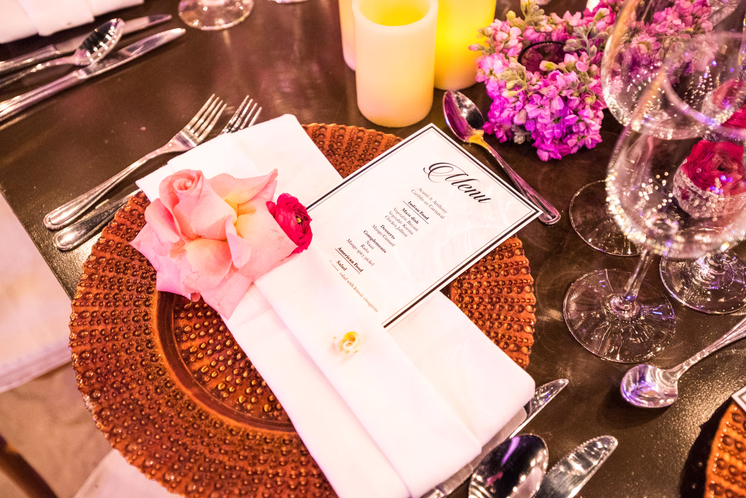 A printed dinner menu and a pale pink flower rest on a gold charger