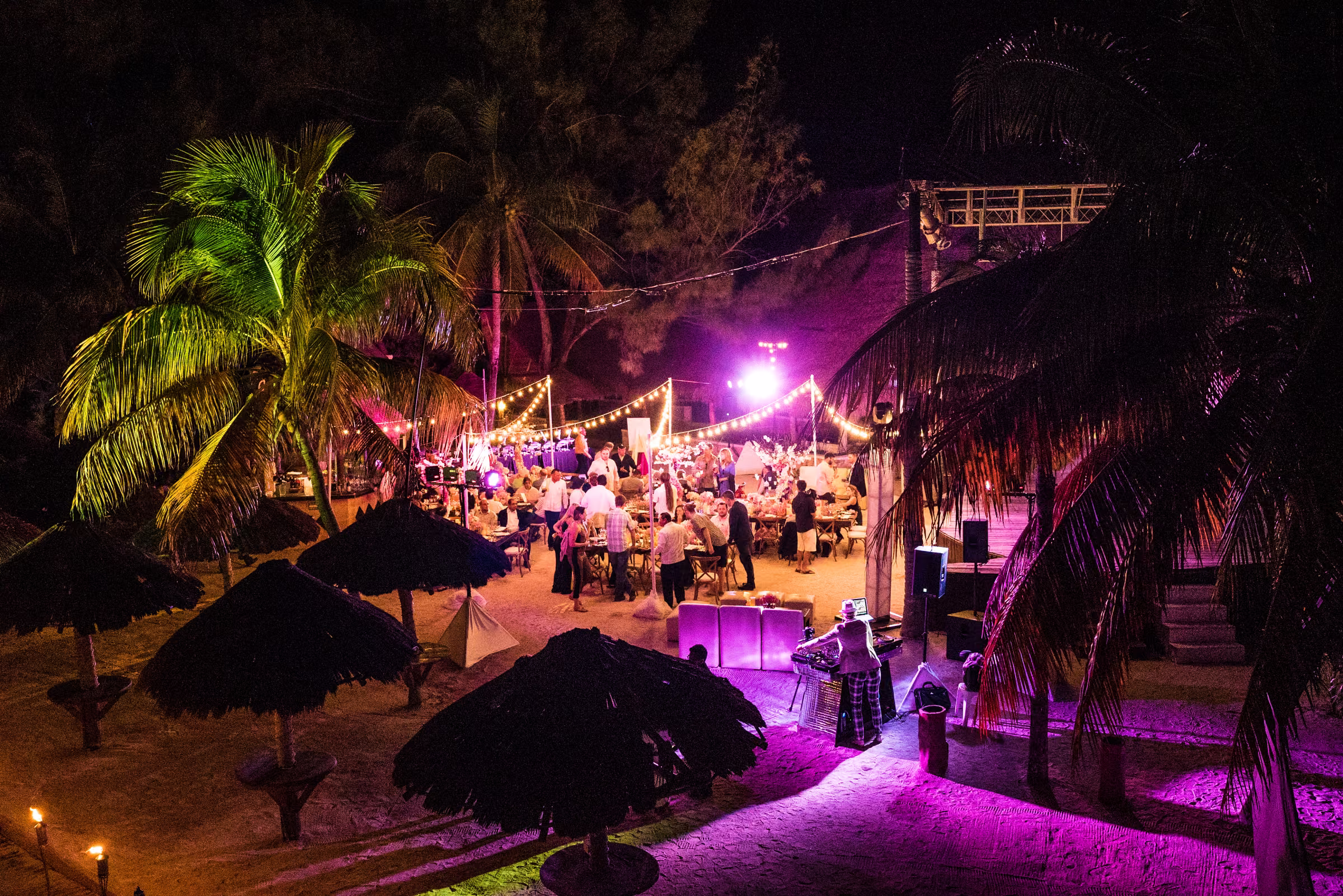 An elevated view shows the illuminated welcome dinner and performance area among palms