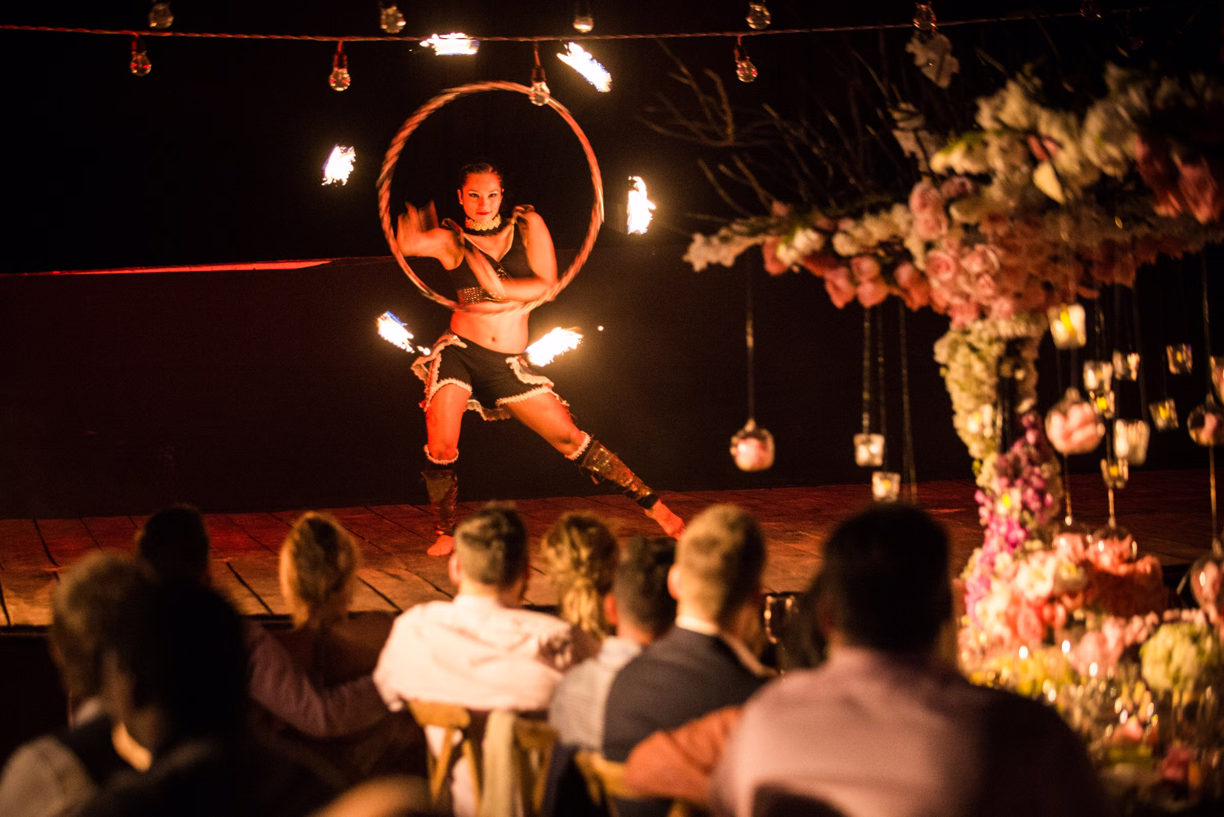 A fire performer spins a flaming hoop in front of seated dinner guests