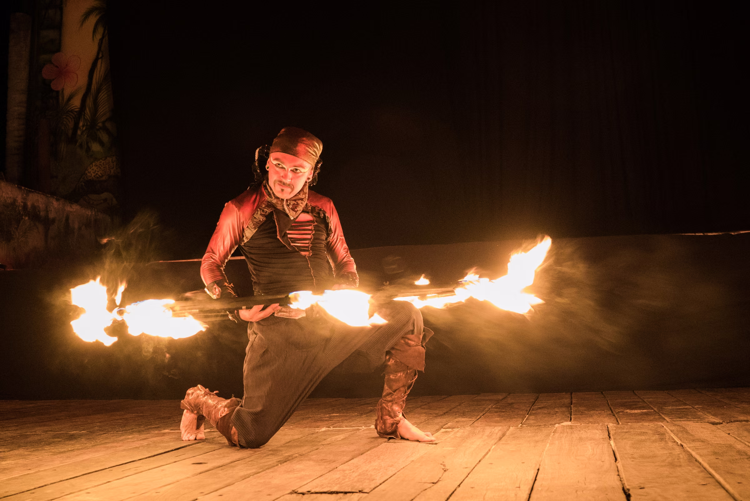 A kneeling fire performer stretches flaming props across the stage