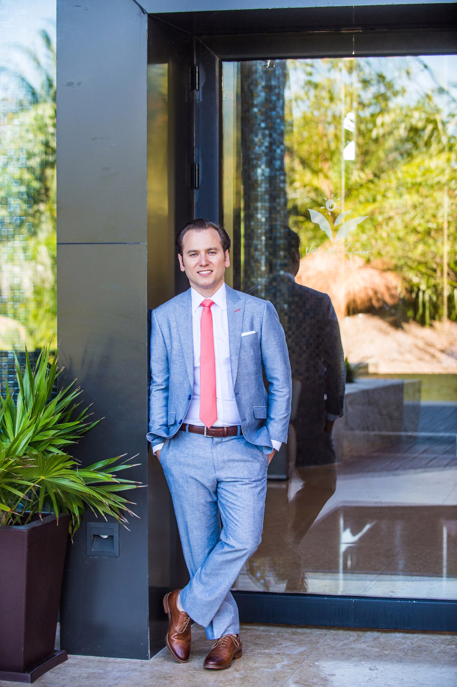 Tony stands in a doorway wearing a light blue suit and pink tie