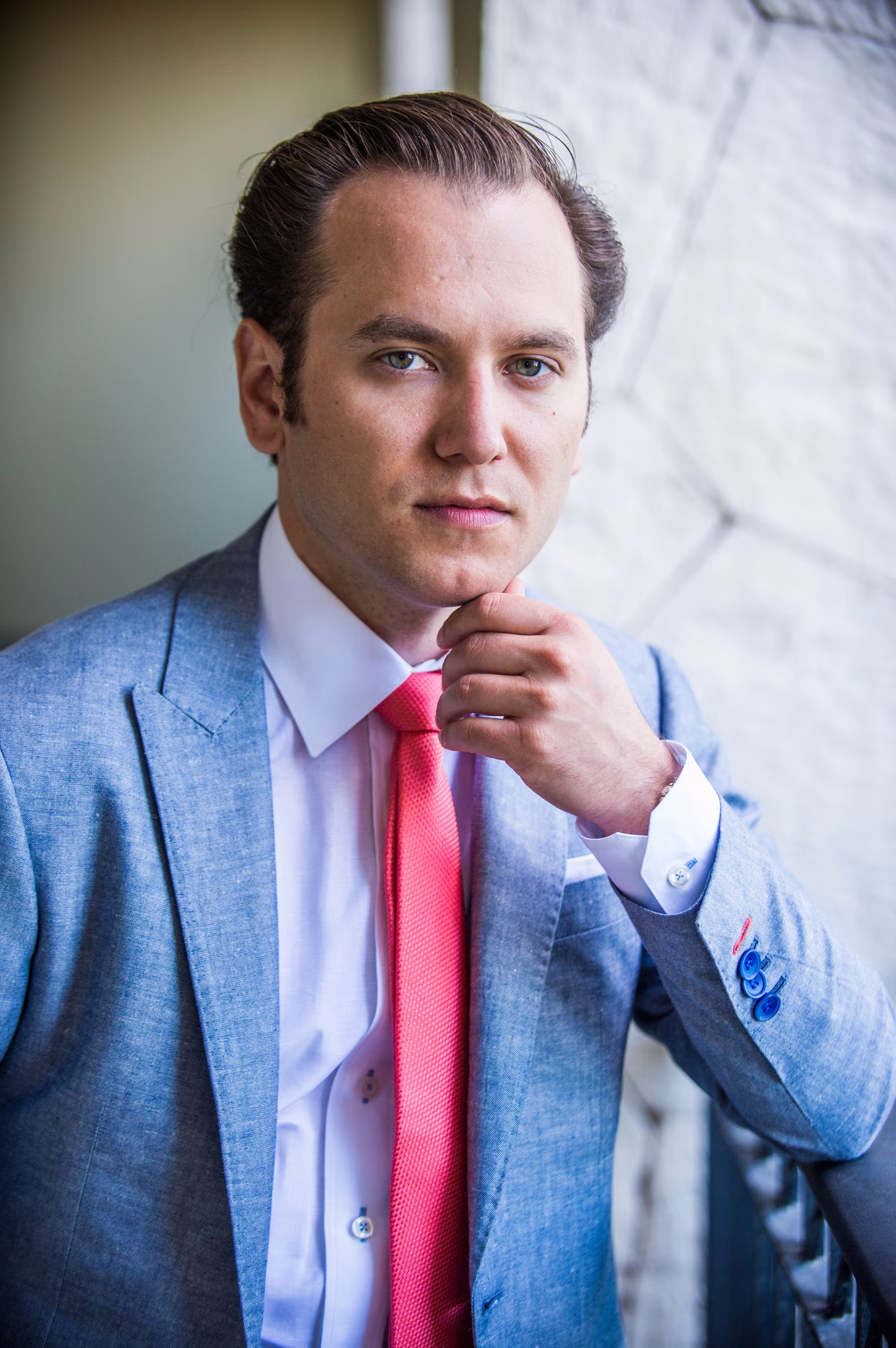 Tony adjusts his pink tie in a close portrait against a pale wall
