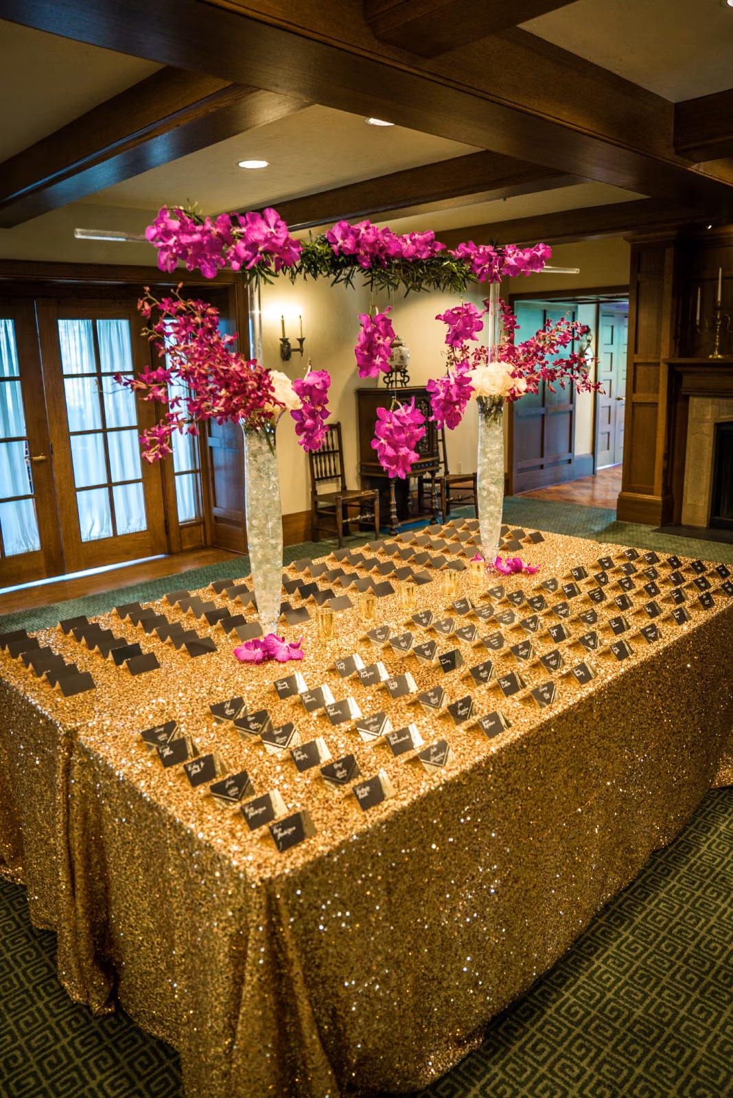 Guest name cards line a gold-covered table beneath vivid pink flowers at Interlachen Country Club
