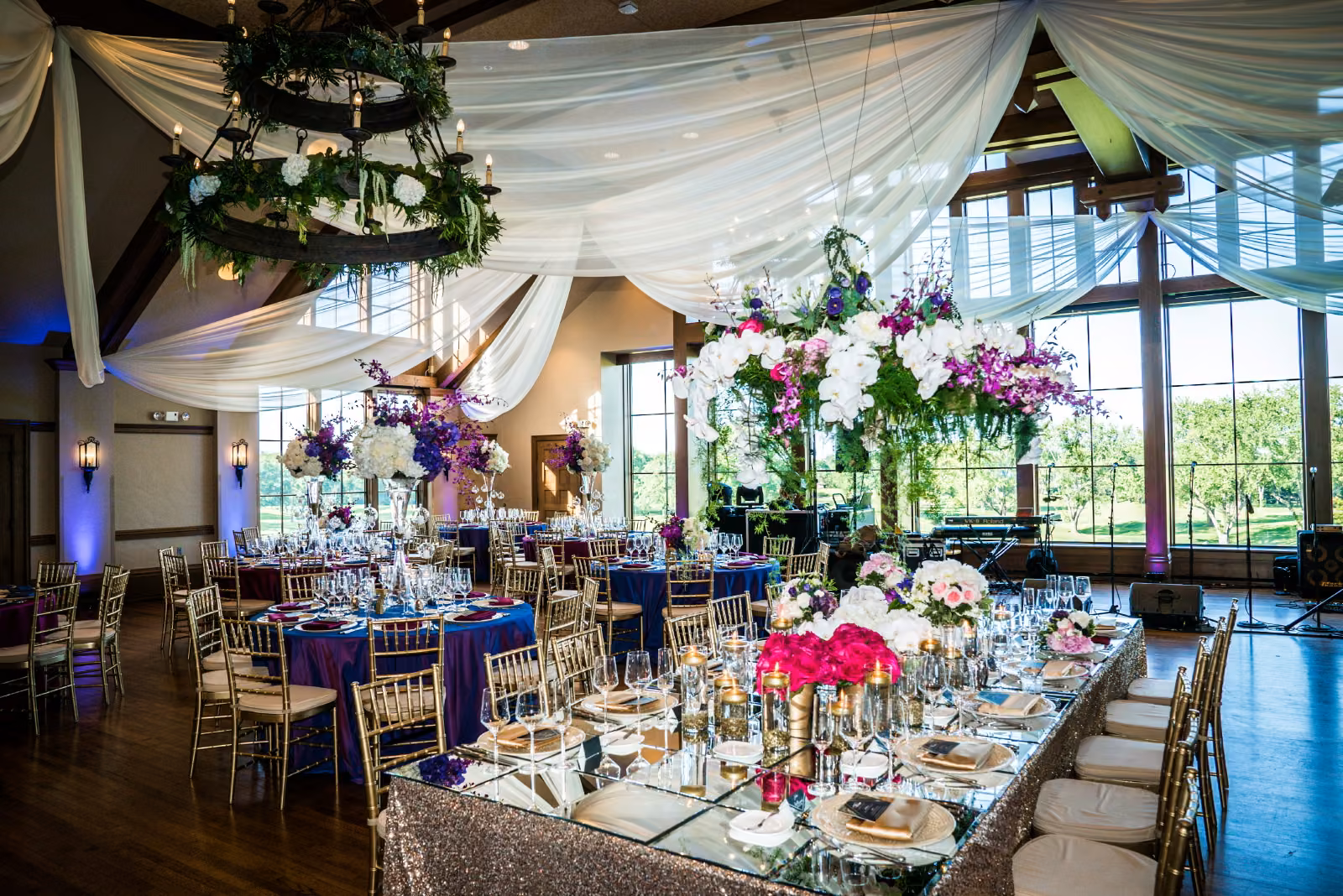 A wide view across the decorated dining room at Interlachen Country Club with gold chairs, purple linens, flowers, and white ceiling draping