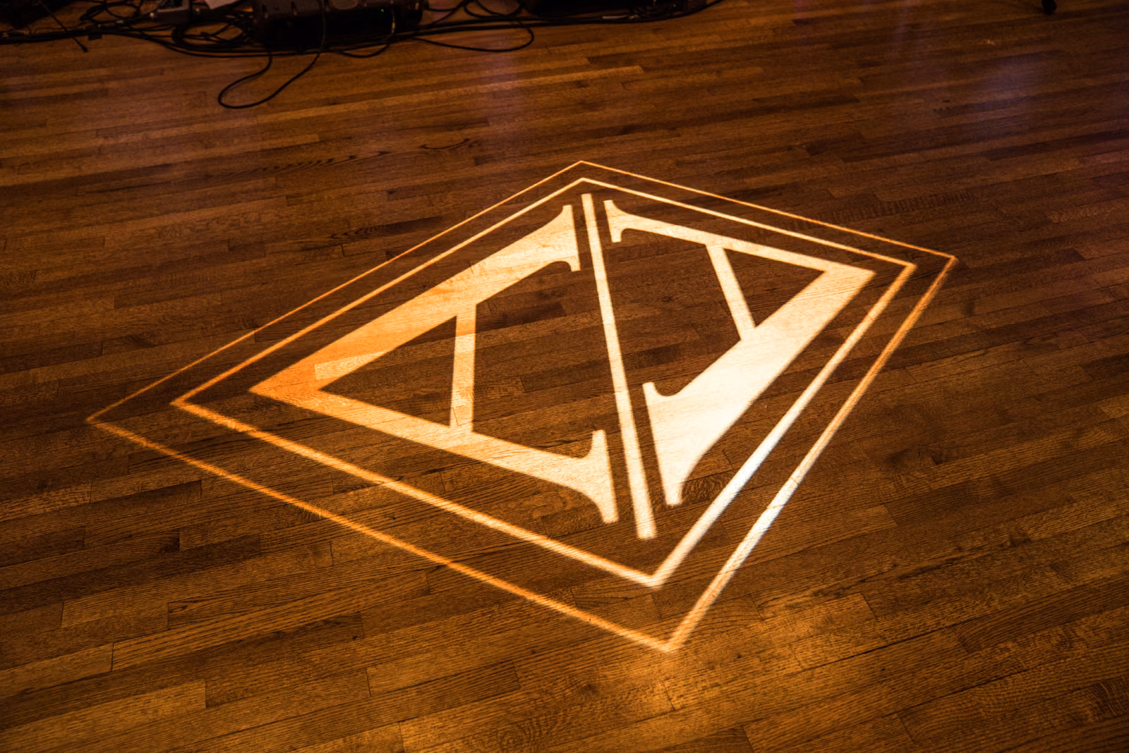 Avanti and Tony’s geometric custom wedding logo is projected in warm light onto the wooden dance floor at Interlachen Country Club