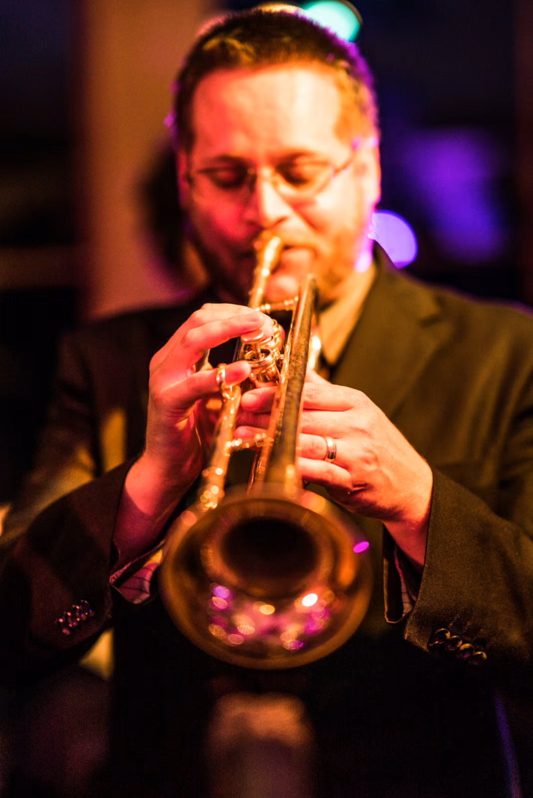 A trumpet player performs in a close portrait under warm and purple stage lighting at Interlachen Country Club