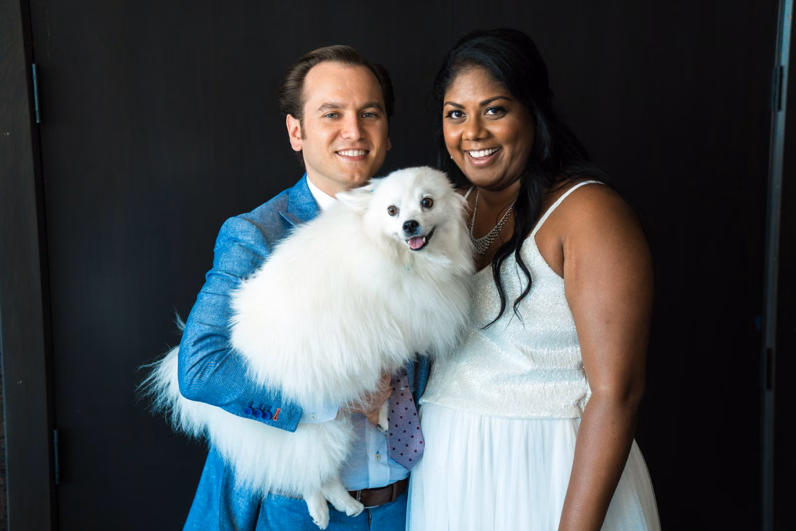 Avanti and Tony smile together while holding their small white dog