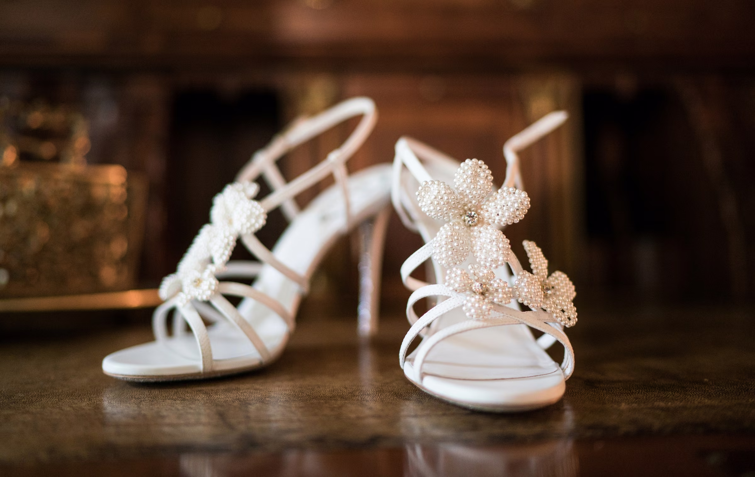 White bridal sandals with jeweled butterfly details rest on a dark wooden surface