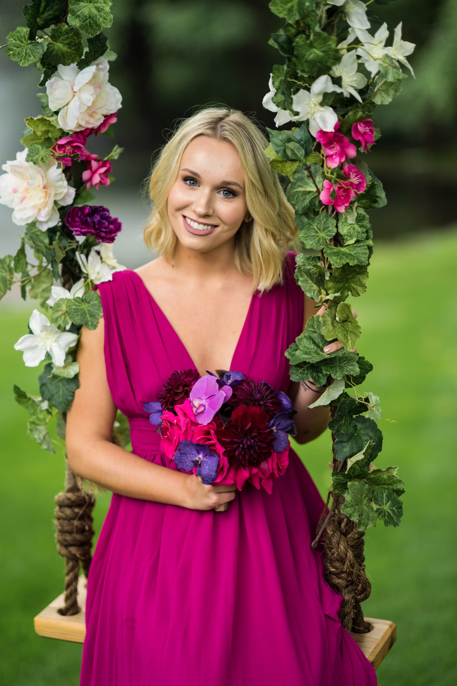 A woman in a pink dress holds flowers while posing on the decorated garden swing