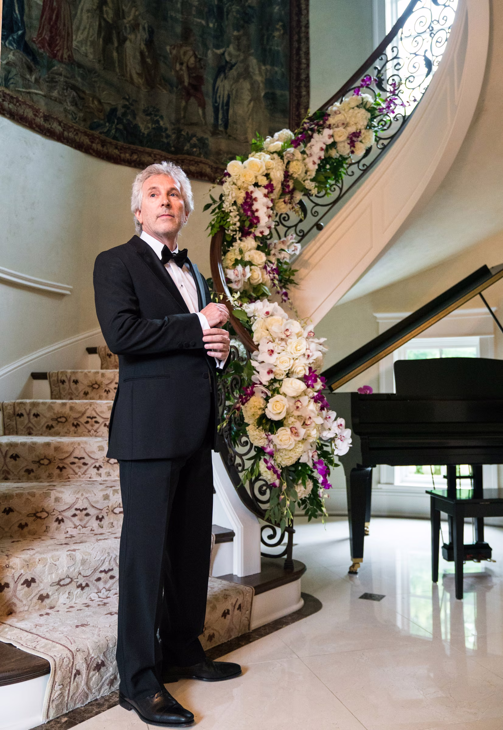 Bill waits in his tuxedo beside the flower-covered staircase