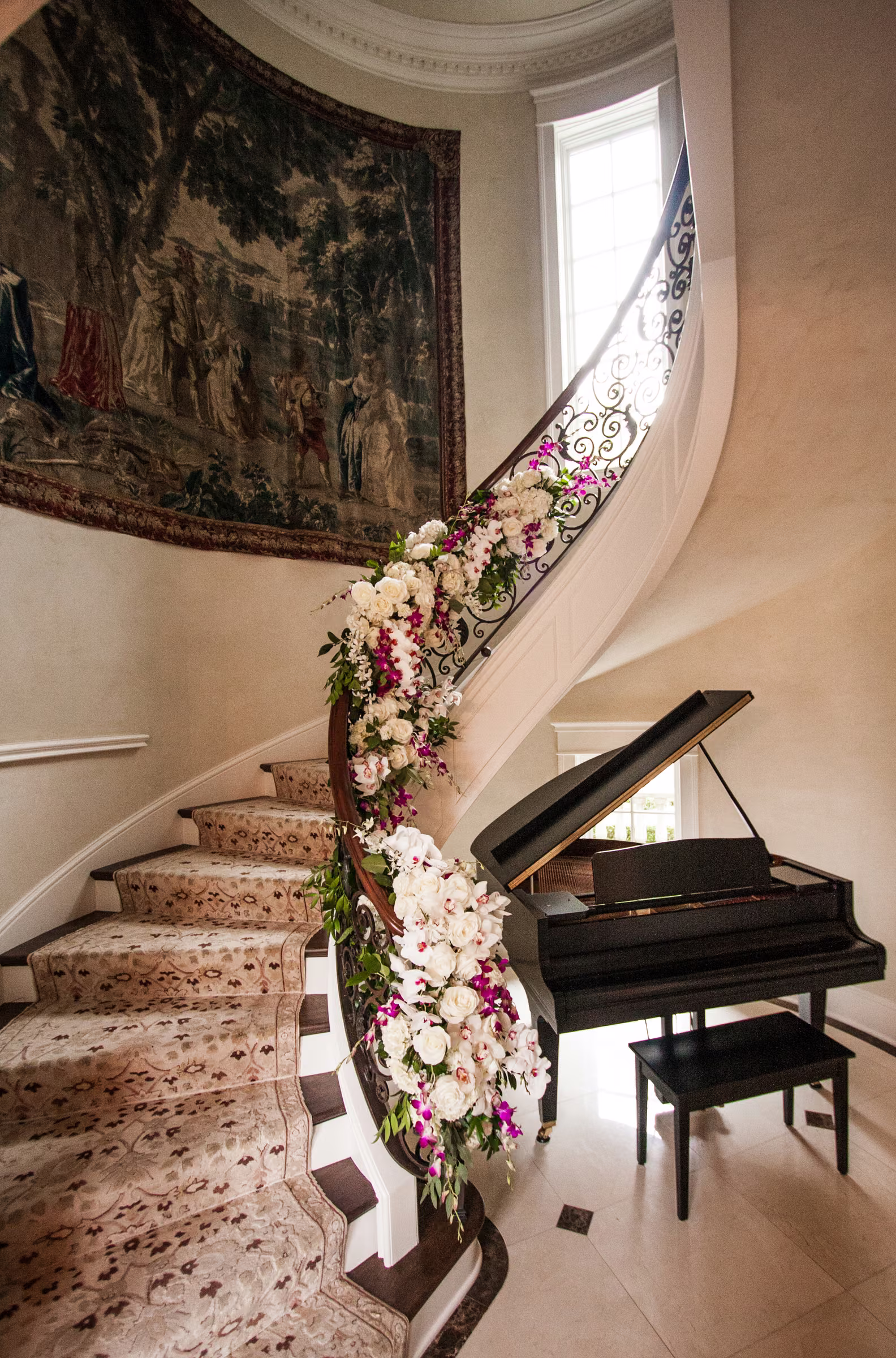 A floral garland follows a curved staircase above a grand piano inside the couple’s home