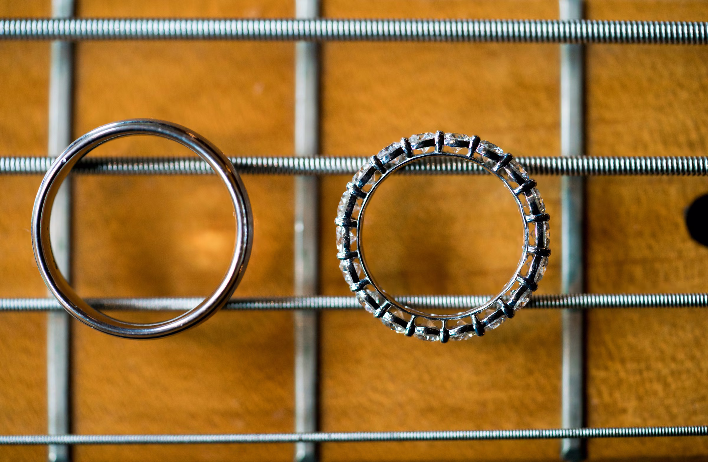 Two wedding rings rest across the strings of a bass guitar in a close overhead photograph