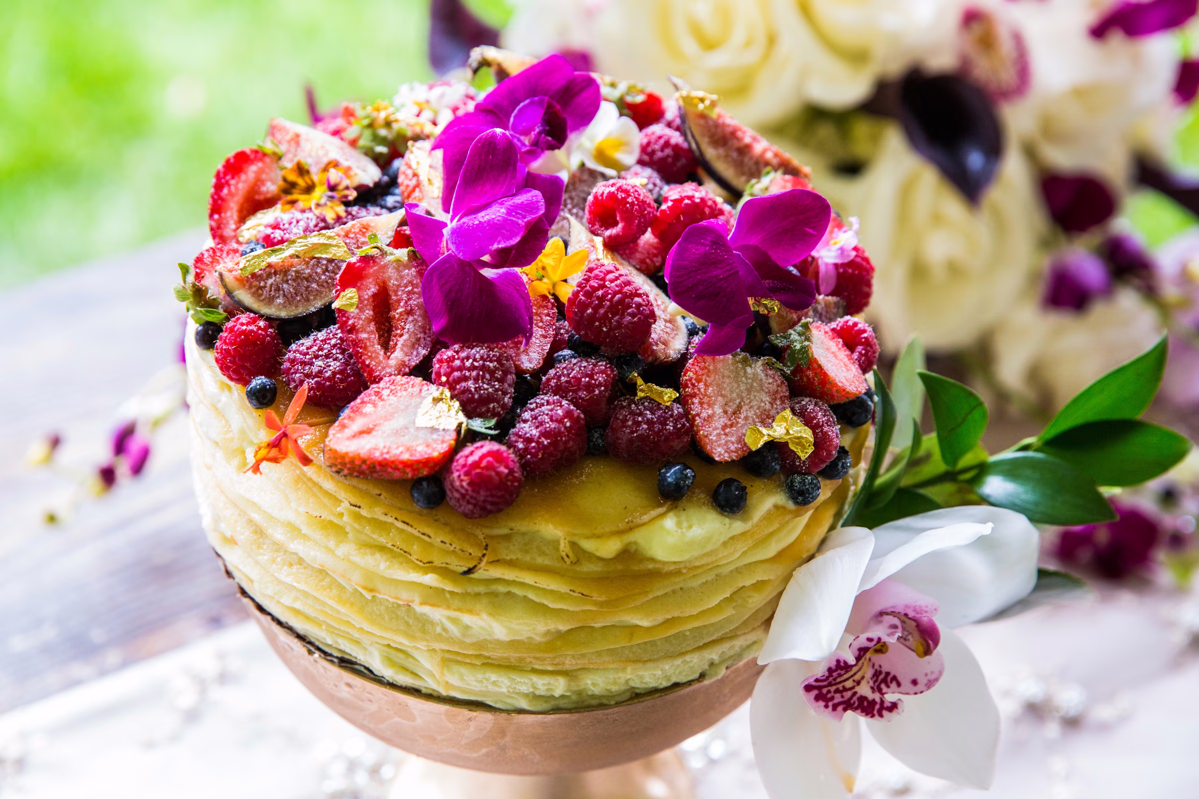 A layered dessert topped with berries and vivid purple flowers sits on the dessert table