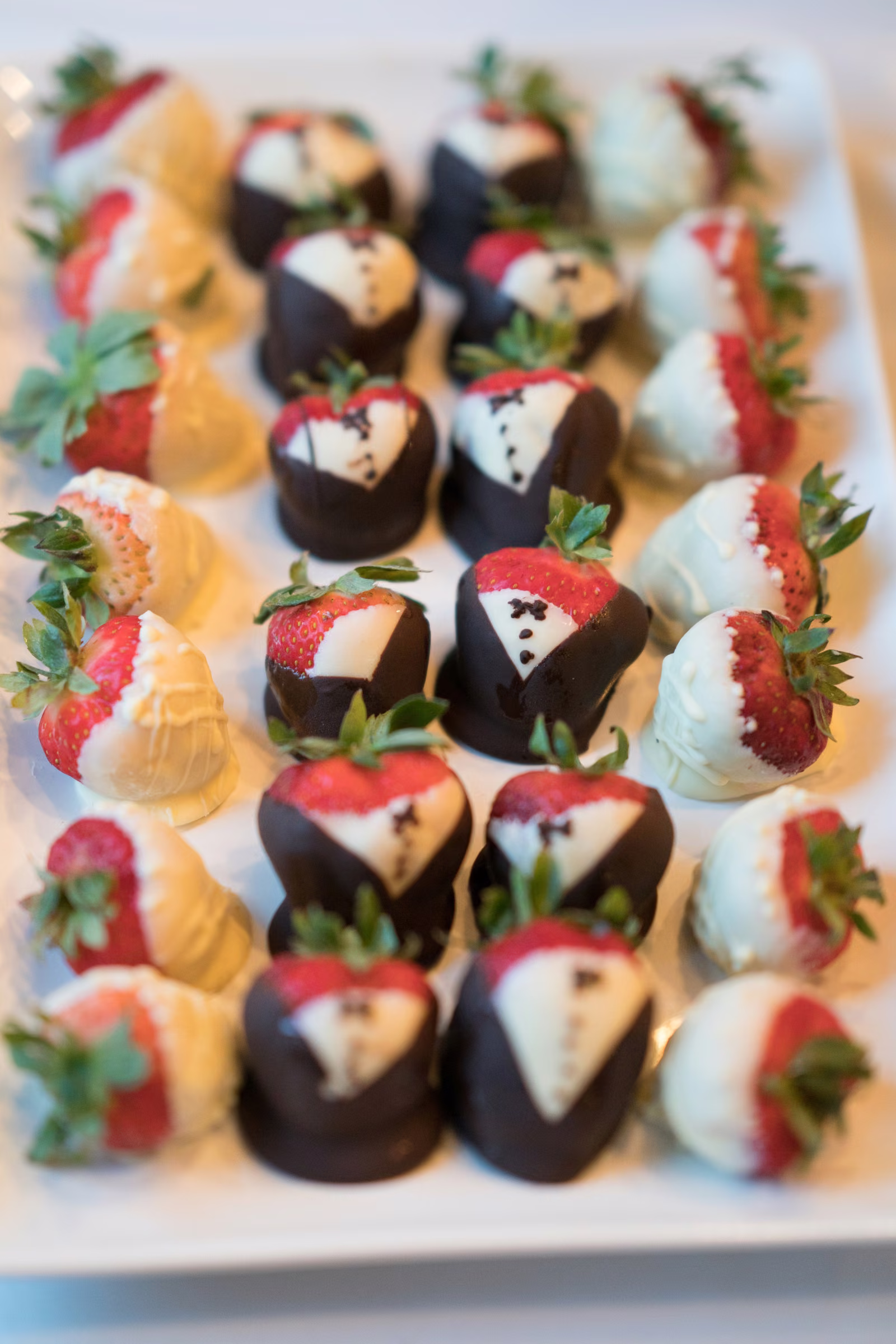 Decorated chocolate-covered strawberries are arranged in rows on a white tray