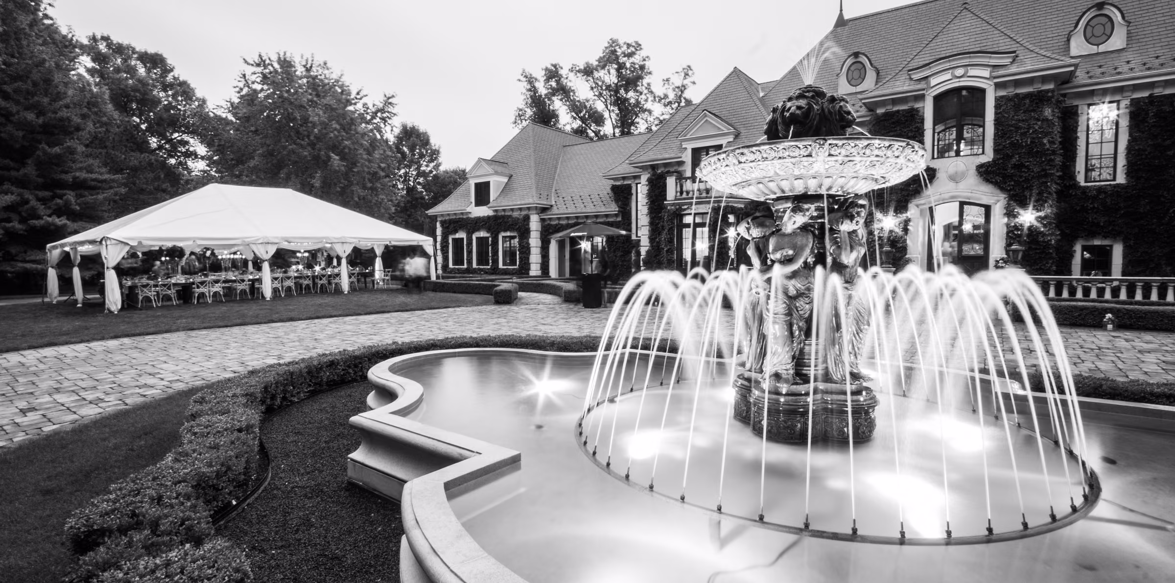 A black and white view shows the estate, reception tent, and fountain with softly blurred water