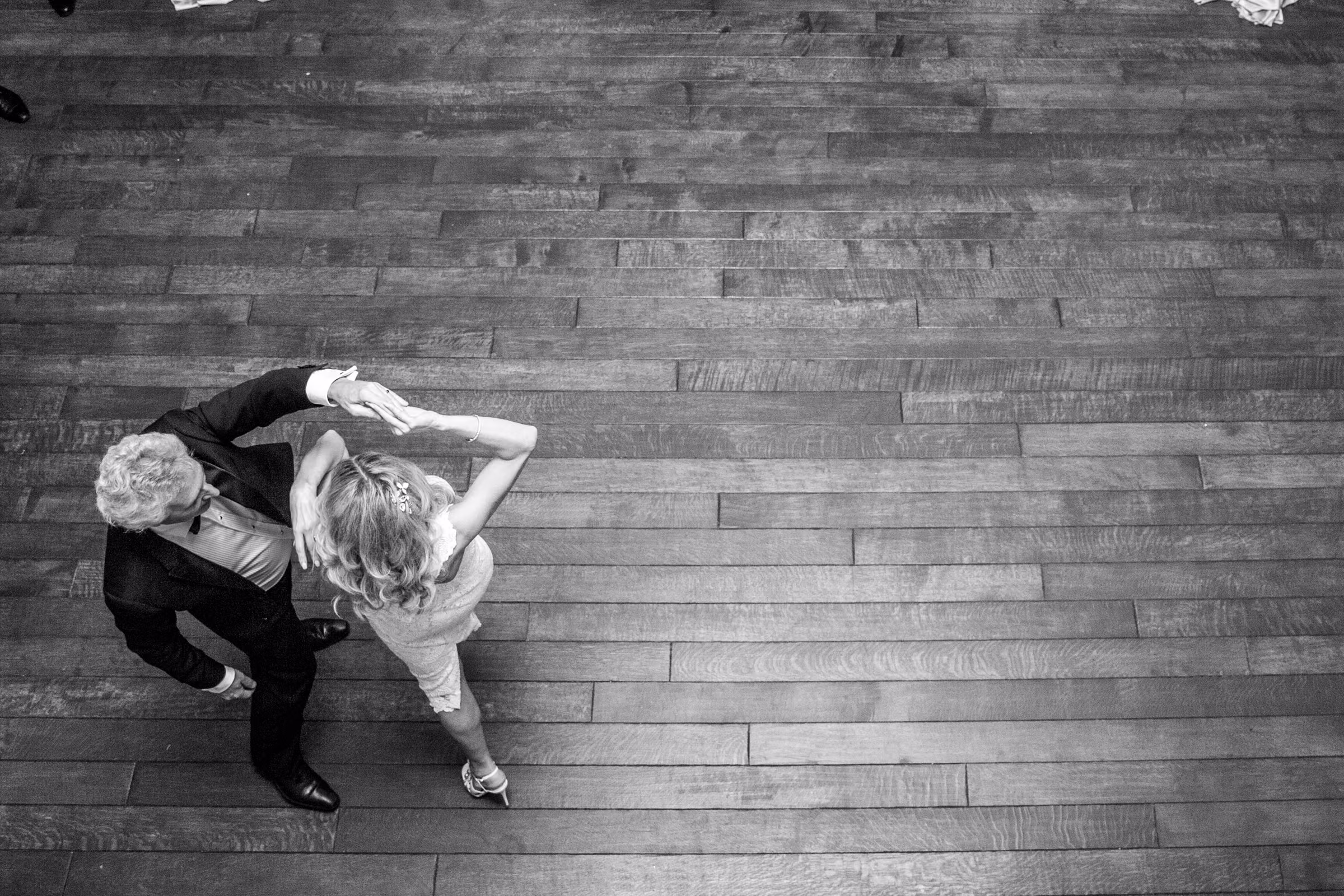 An overhead black and white photograph shows Bill and Daiva dancing across a clear wooden floor