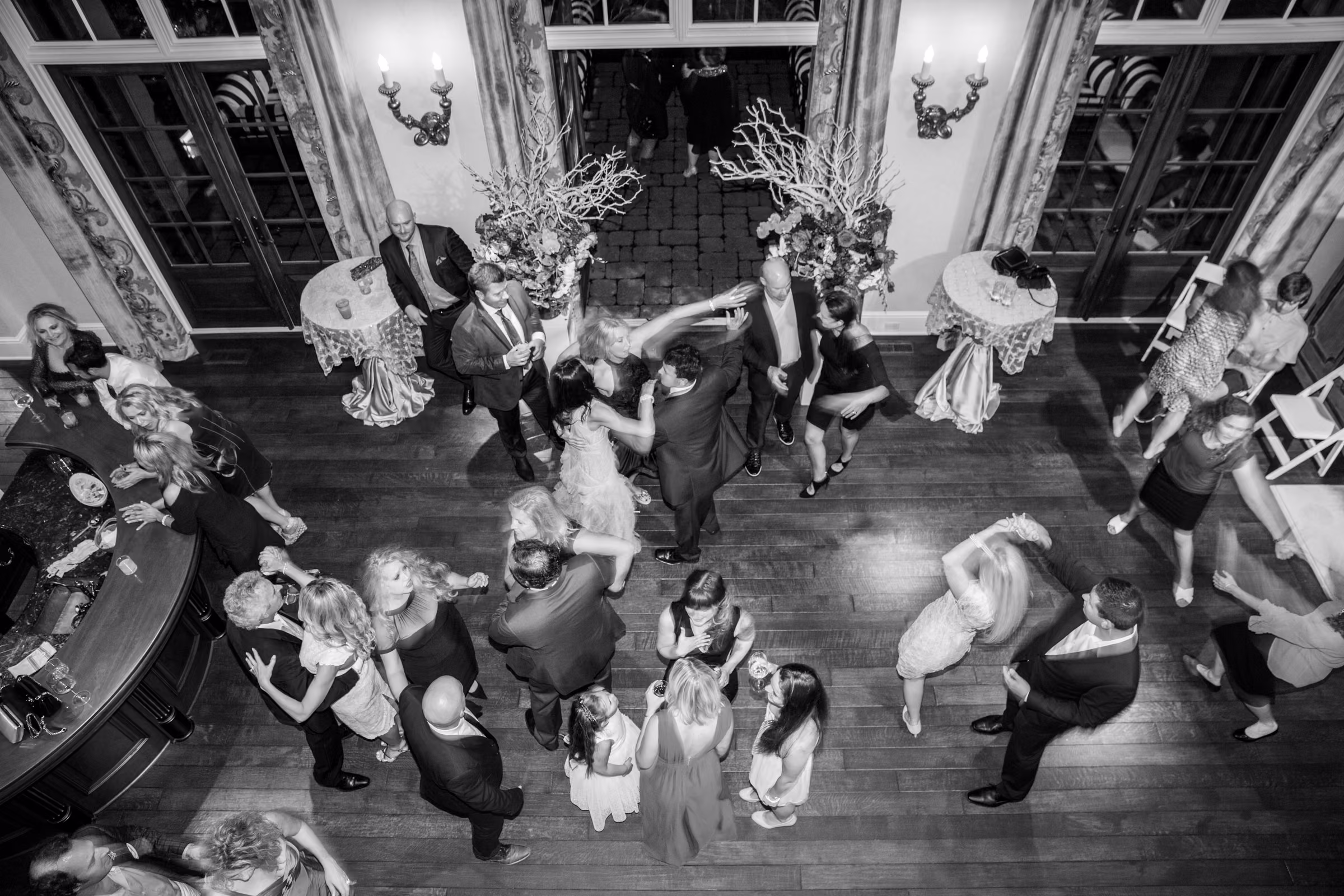 An overhead black and white view shows wedding guests dancing together inside the estate