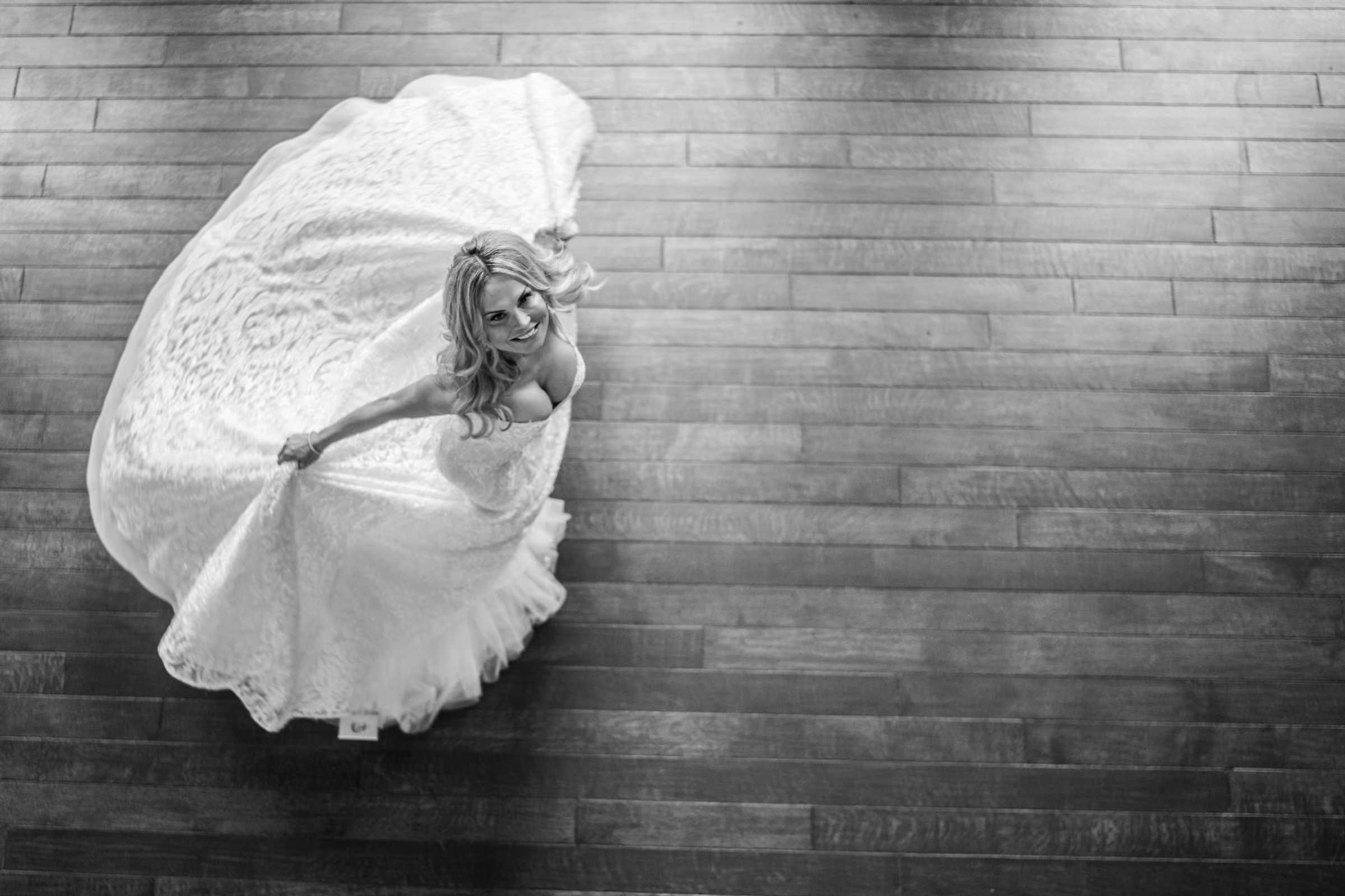 An overhead black and white photograph shows Daiva turning in her wedding dress on a wooden floor