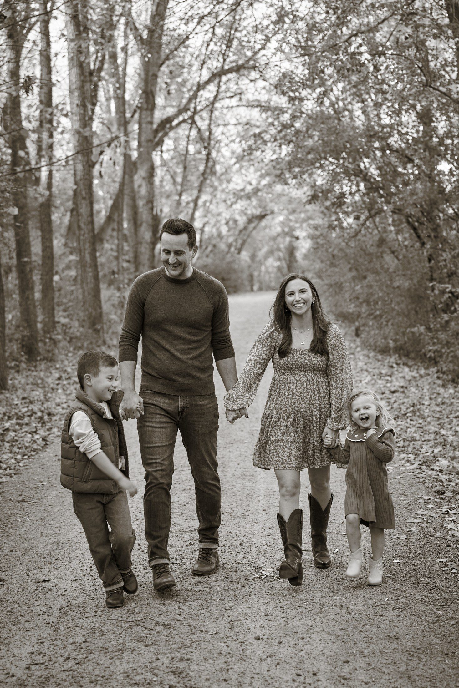 Black and white portrait of the Engle family walking hand in hand along a wooded lane in Orono, Minnesota
