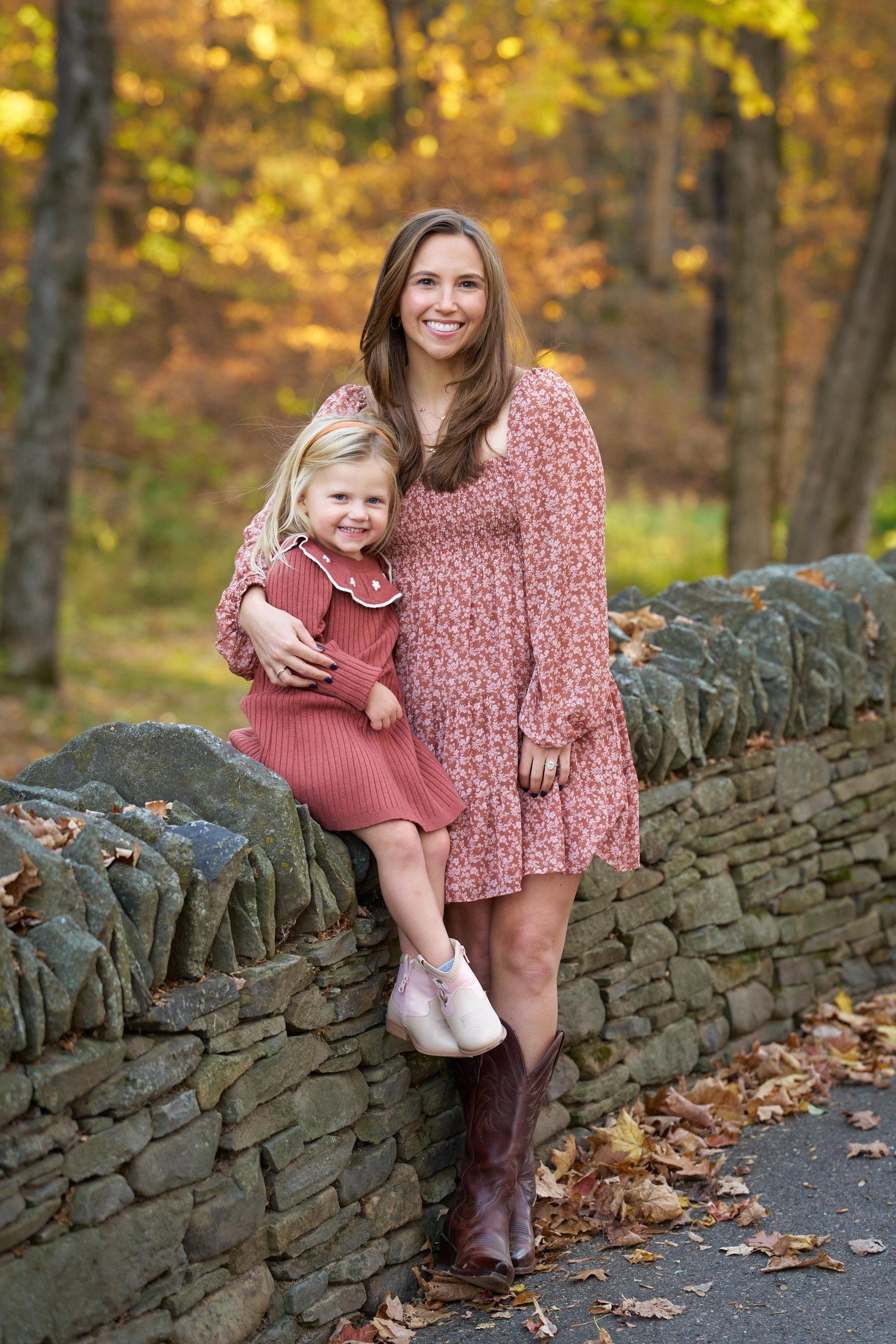Beth Engle and her daughter beside a stone wall with autumn color in Orono, Minnesota