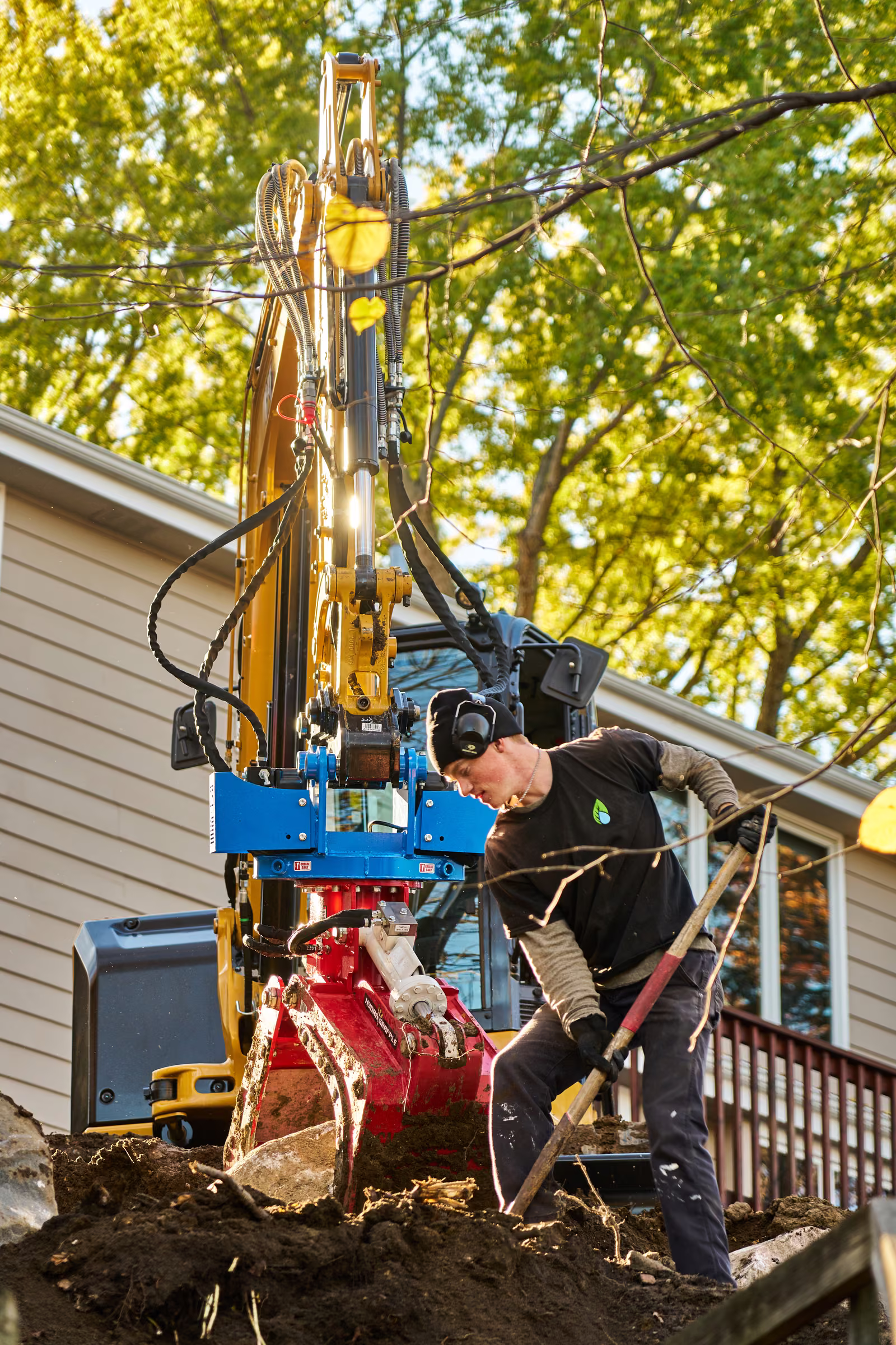 A Freshwater Landscaping crew member uses a shovel beside the excavator’s red grapple