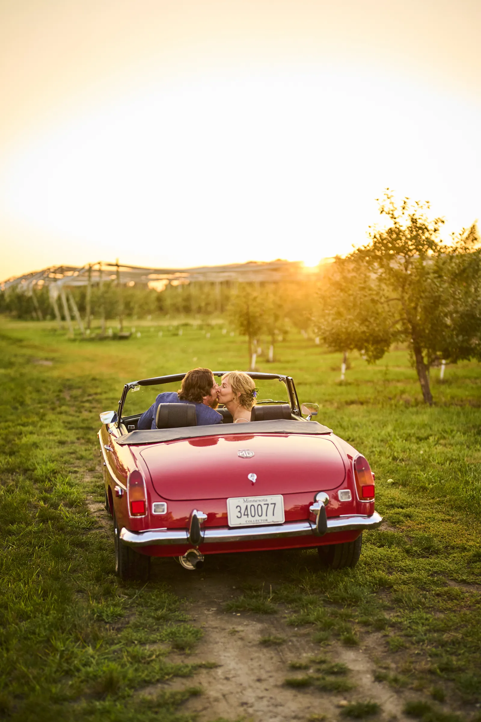 Jeanne and Brian kiss in a red convertible between orchard rows as the sun sets behind them, Ashery Lane Farm, Mayer, Minnesota