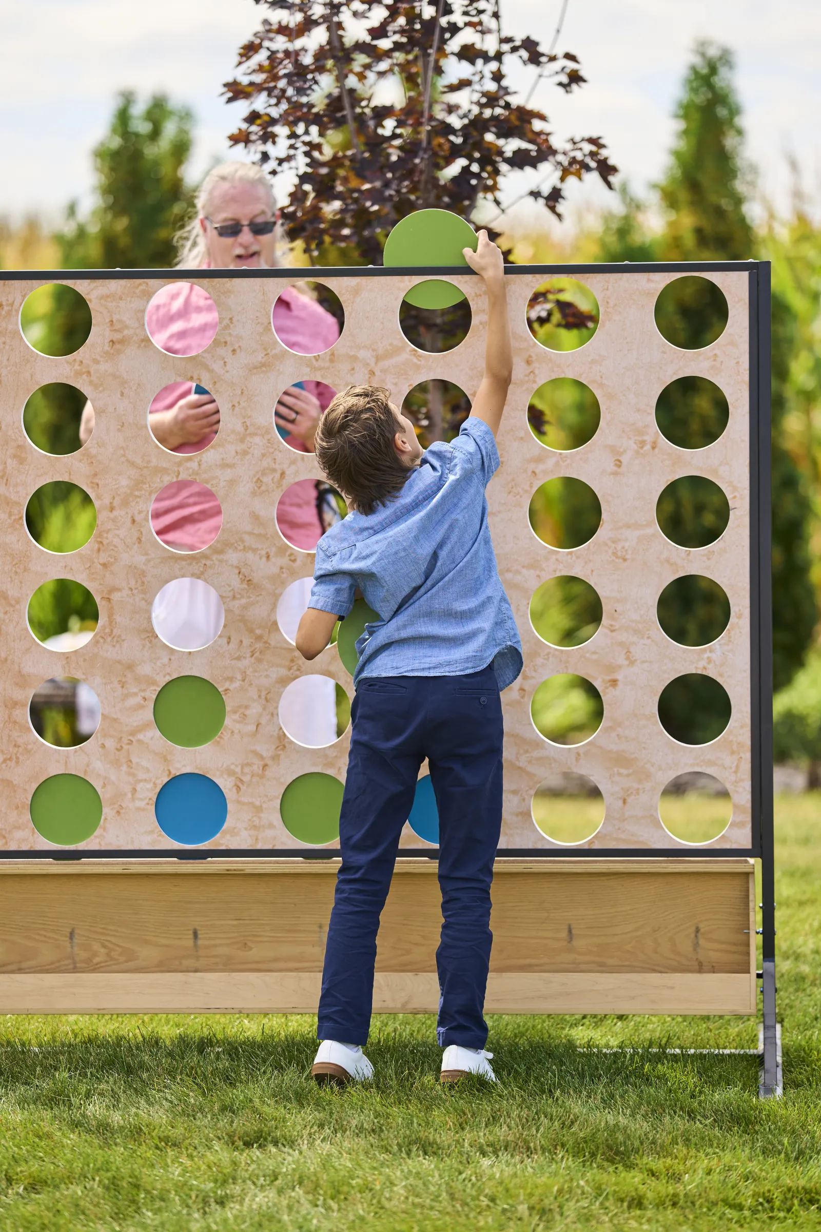 A young guest reaches up to place a disc in an oversized four-in-a-row lawn game, Ashery Lane Farm, Mayer, Minnesota