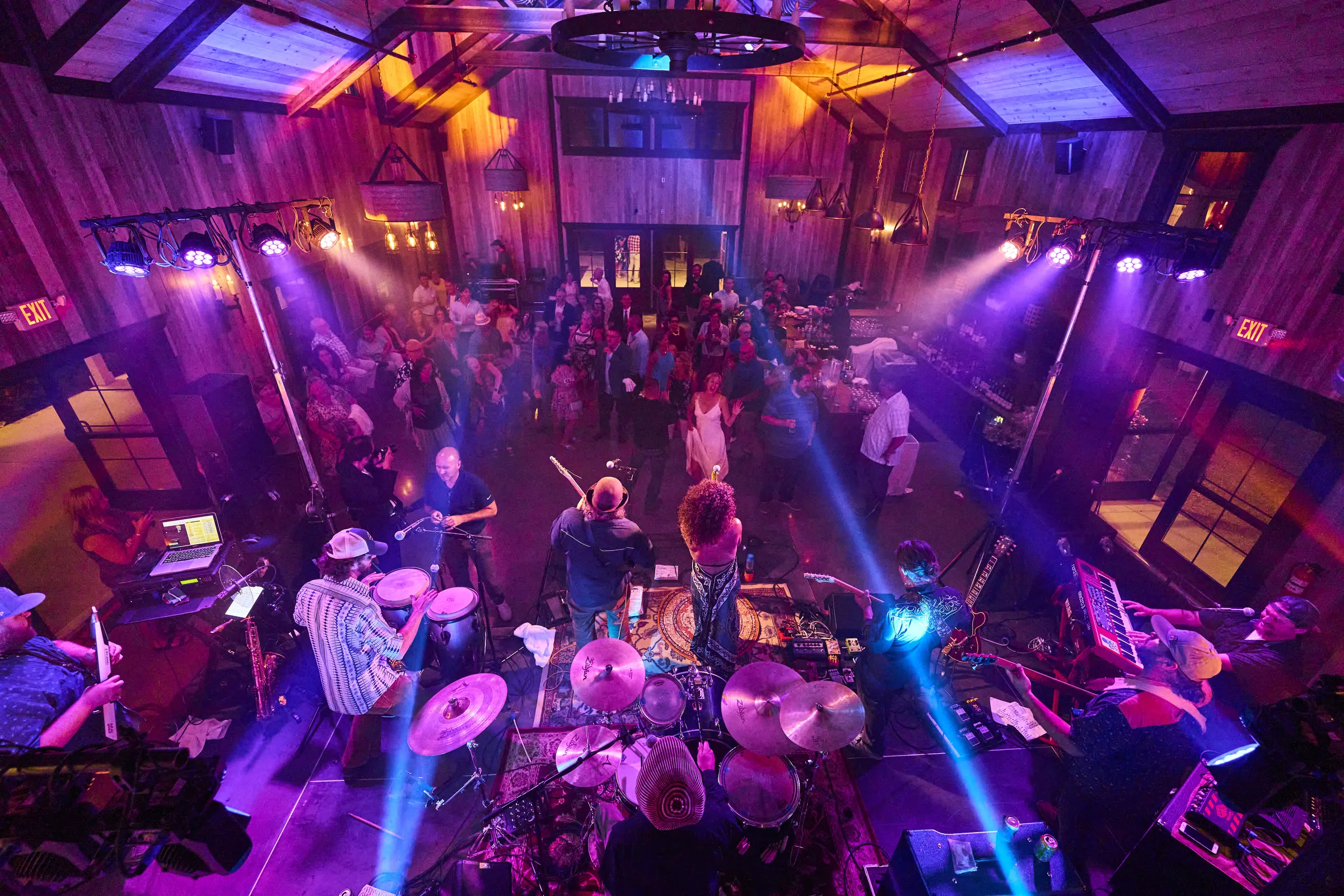 An elevated view of wedding guests celebrating beneath vivid pink and purple lights in the reception barn, Ashery Lane Farm, Mayer, Minnesota