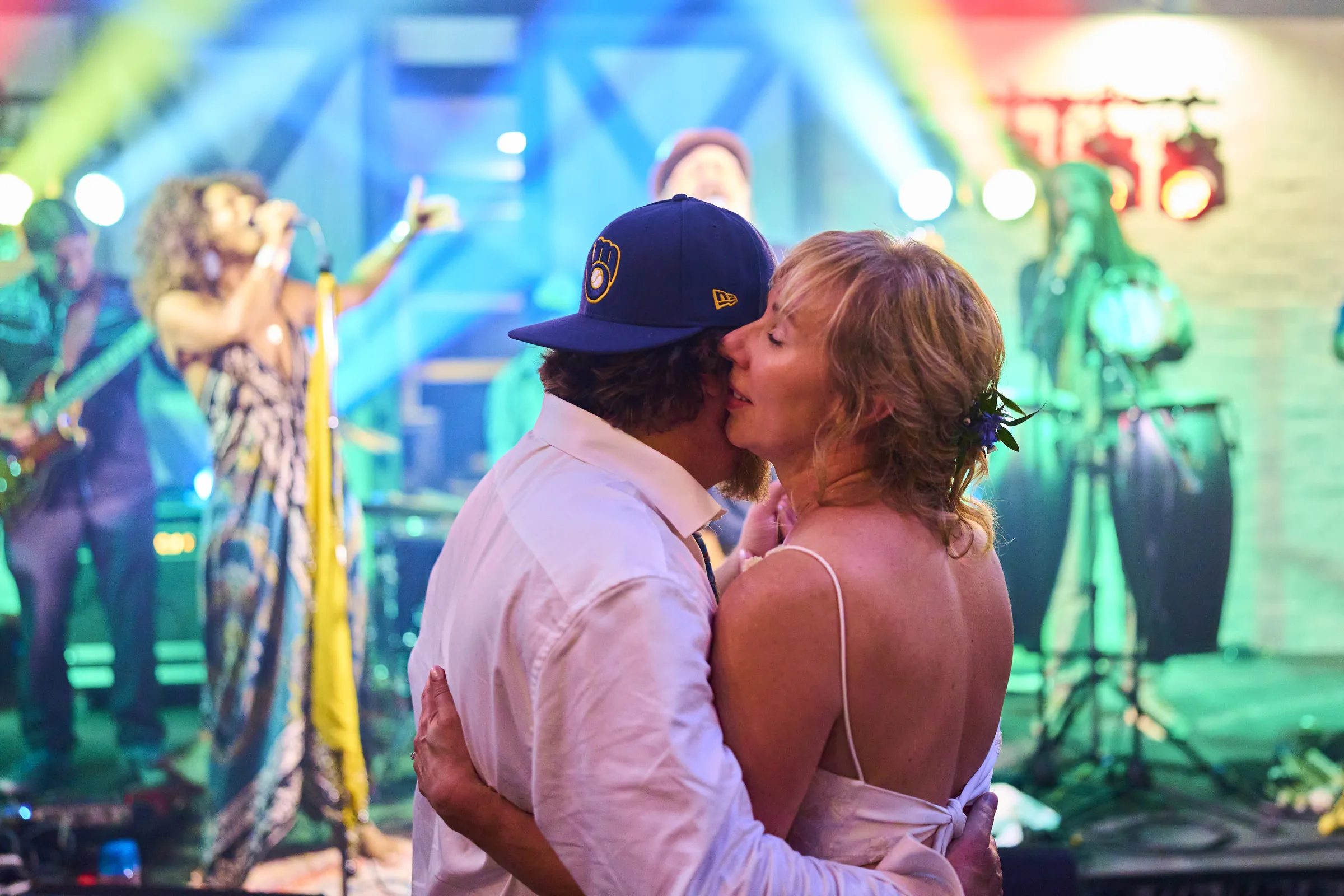 Jeanne and Brian kiss on the dance floor while the band performs behind them under colorful lights, Ashery Lane Farm, Mayer, Minnesota