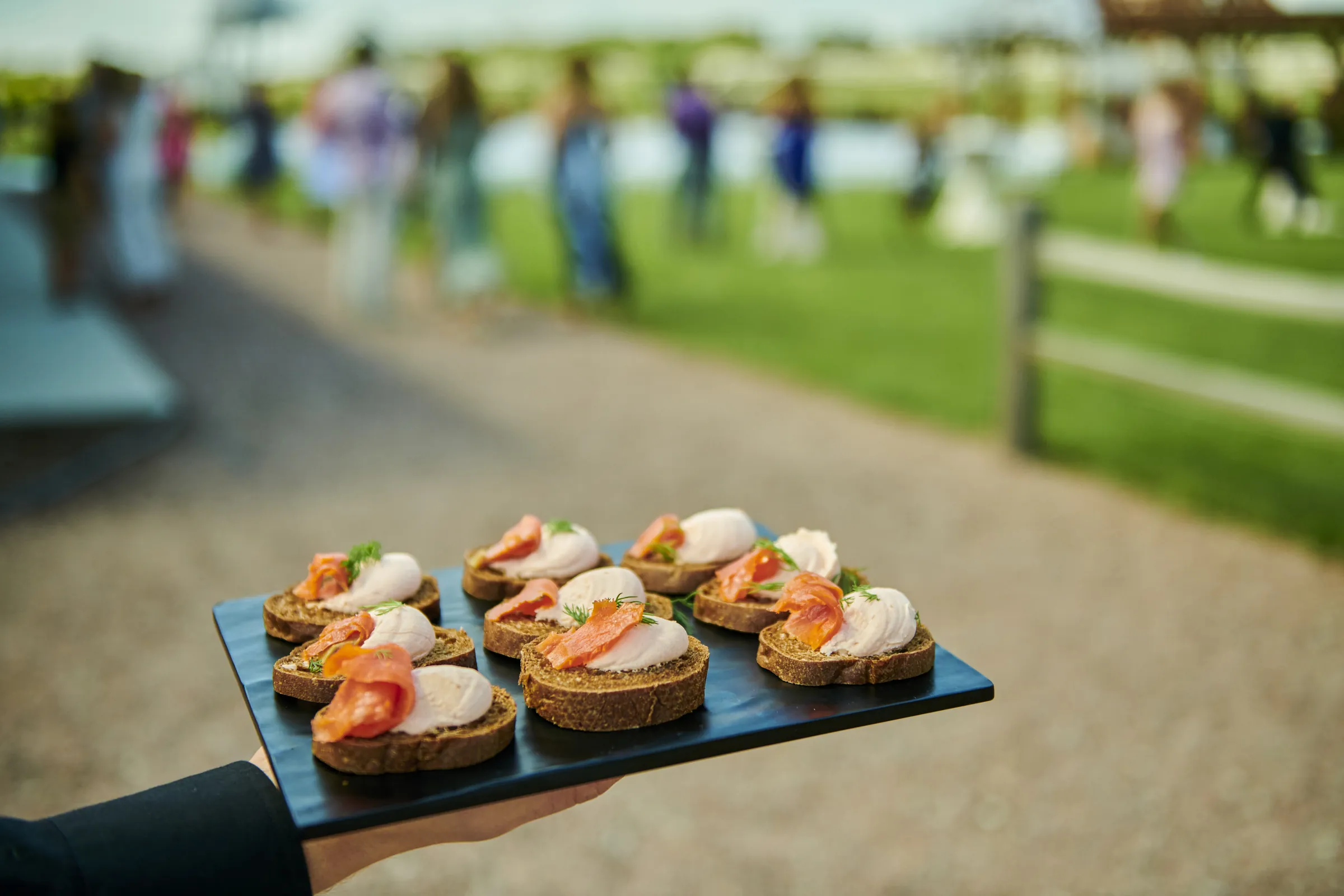 A tray of small appetizers held in the foreground while wedding guests gather on the lawn, Ashery Lane Farm, Mayer, Minnesota