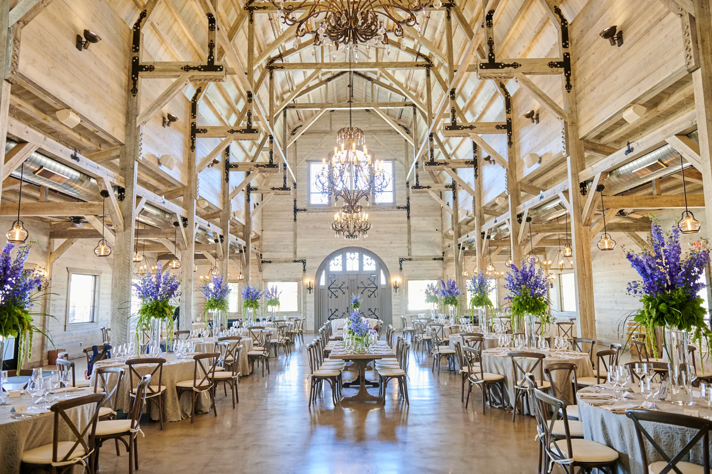 The reception barn at Ashery Lane Farm with wooden tables, blue flowers, chandeliers, and a central aisle, Ashery Lane Farm, Mayer, Minnesota