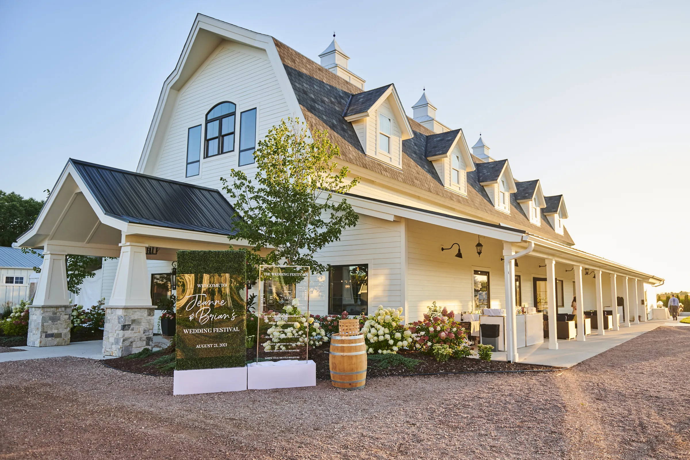 An angled evening view of the white reception barn and its long covered porch at Ashery Lane Farm, Ashery Lane Farm, Mayer, Minnesota